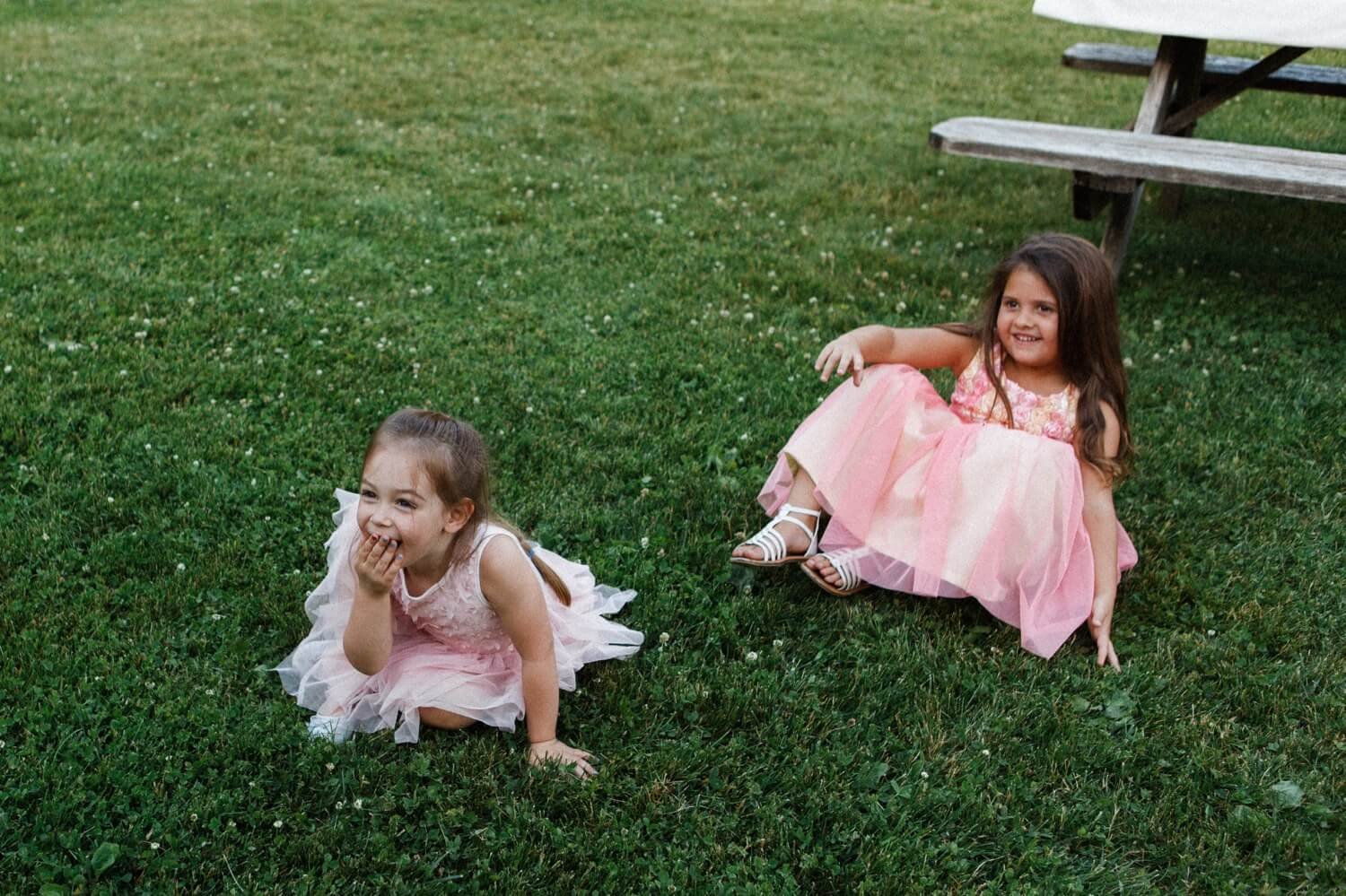 073_Mount Hood Organic Farms Wedding-Two girls in pink dresses sit in grass and laugh.jpg