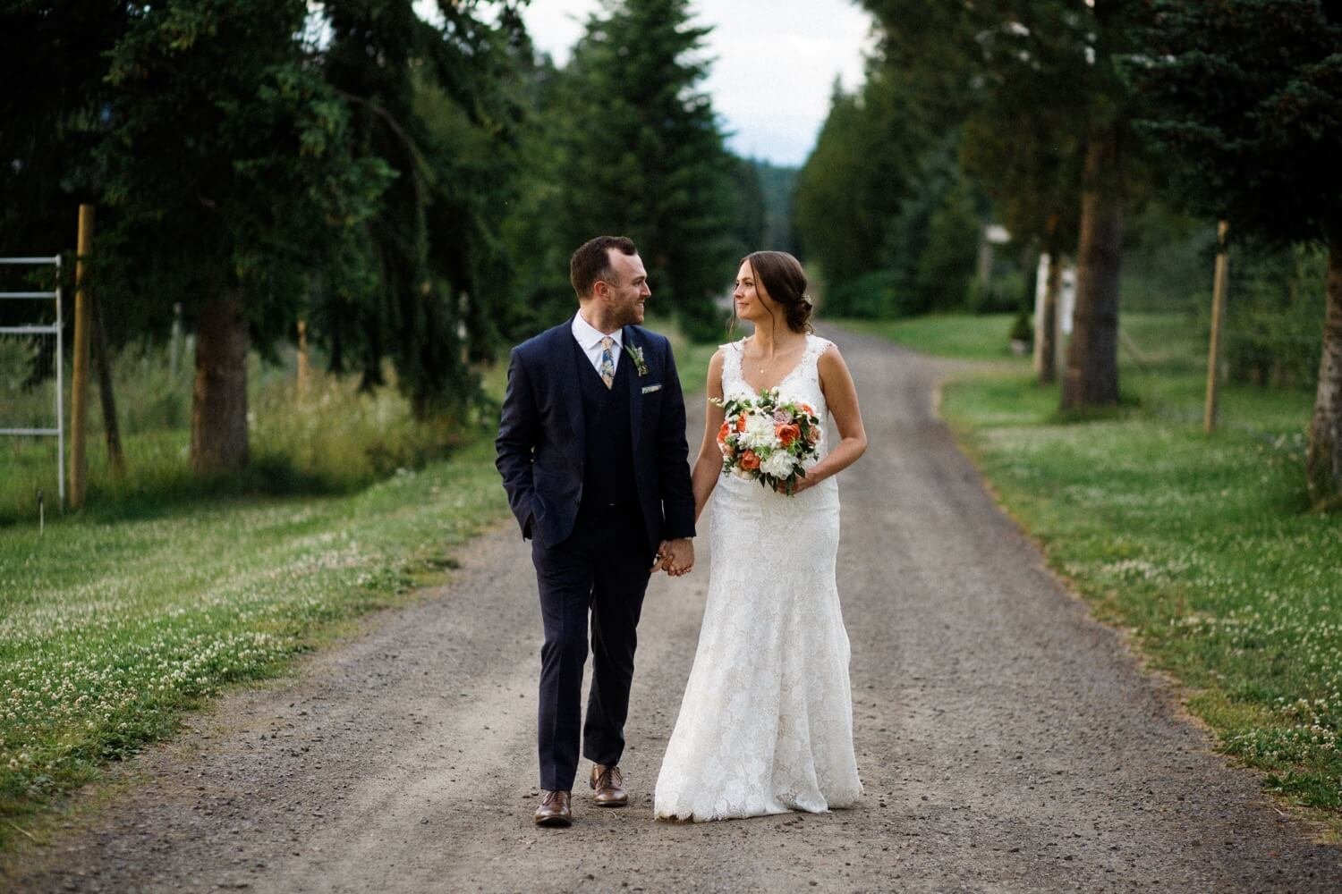099_Mount Hood Organic Farms Wedding-Bride and groom hold hands and walk together down gravel road.jpg