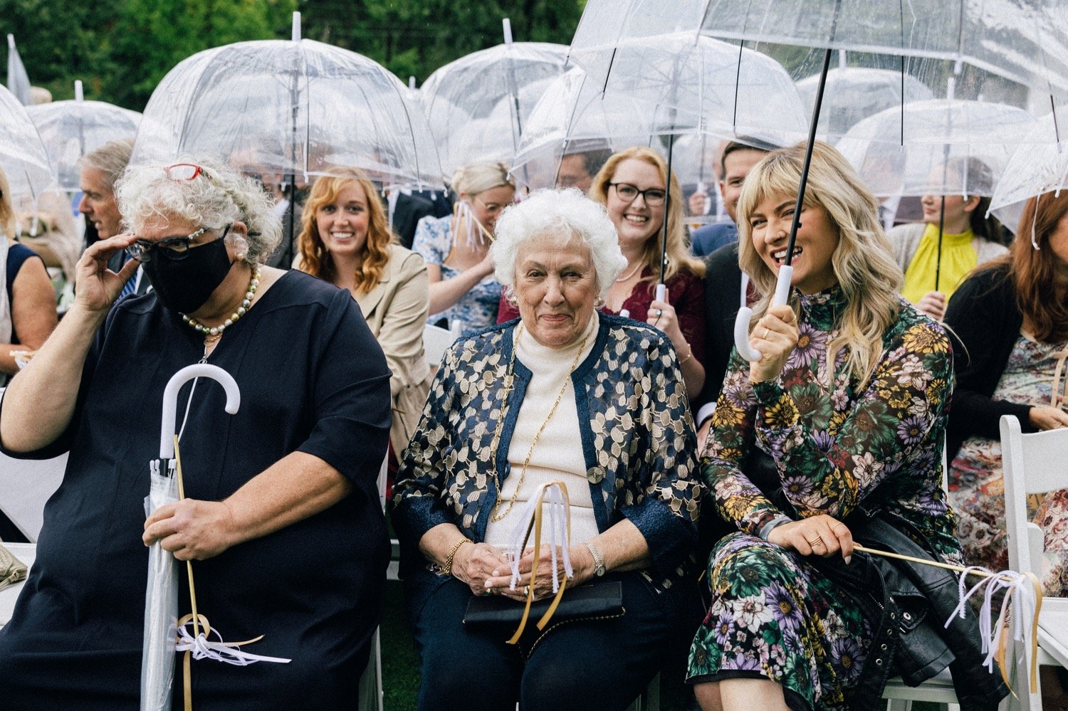  Women watch wedding ceremony while holding clear umbrellas 