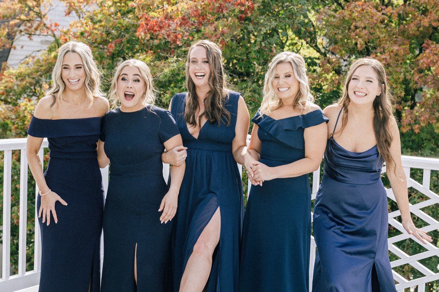 Five women in navy blue dresses hold hands and smile 