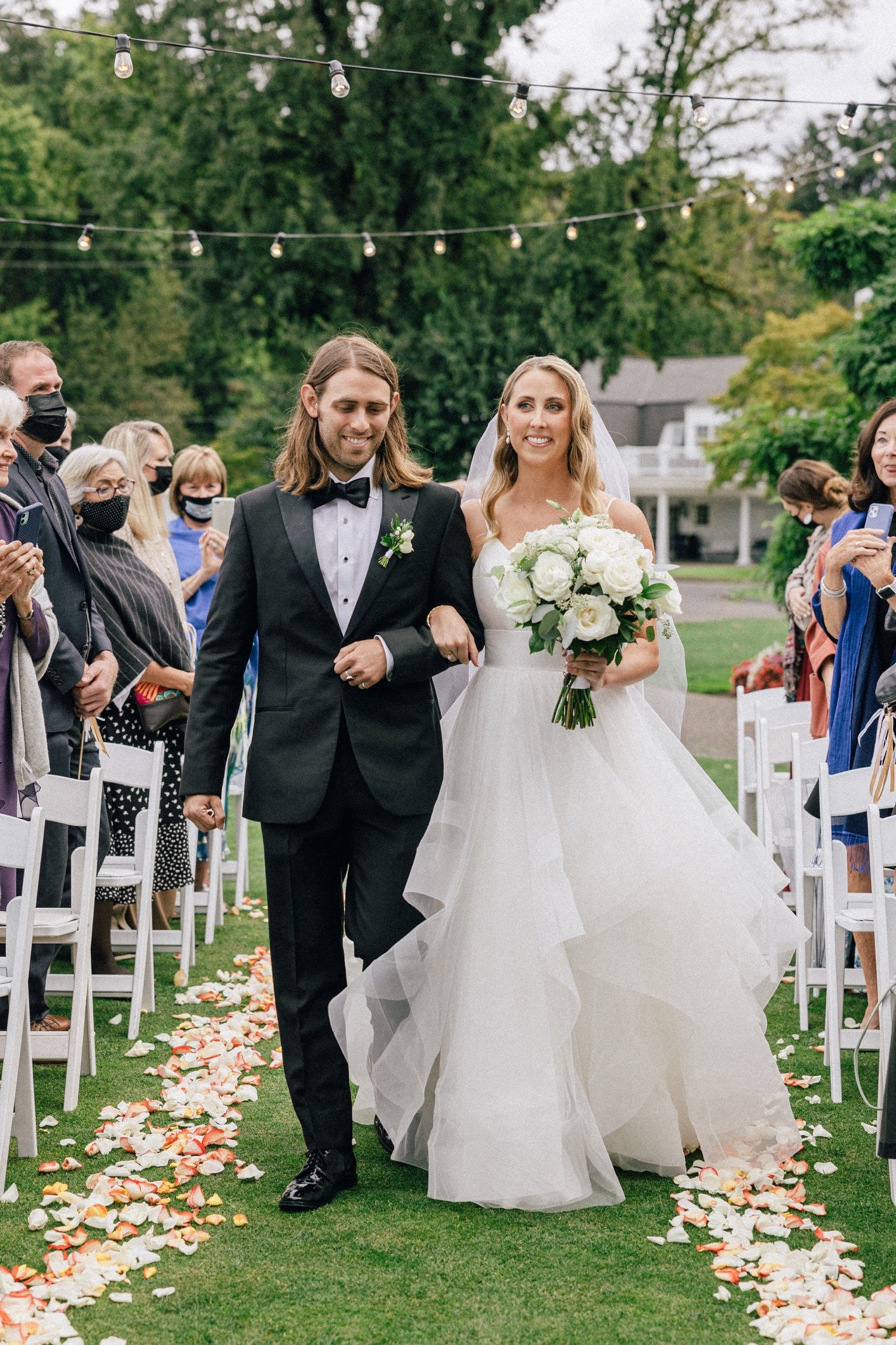  Bride walks down wedding aisle with man wearing black suit and bowtie 
