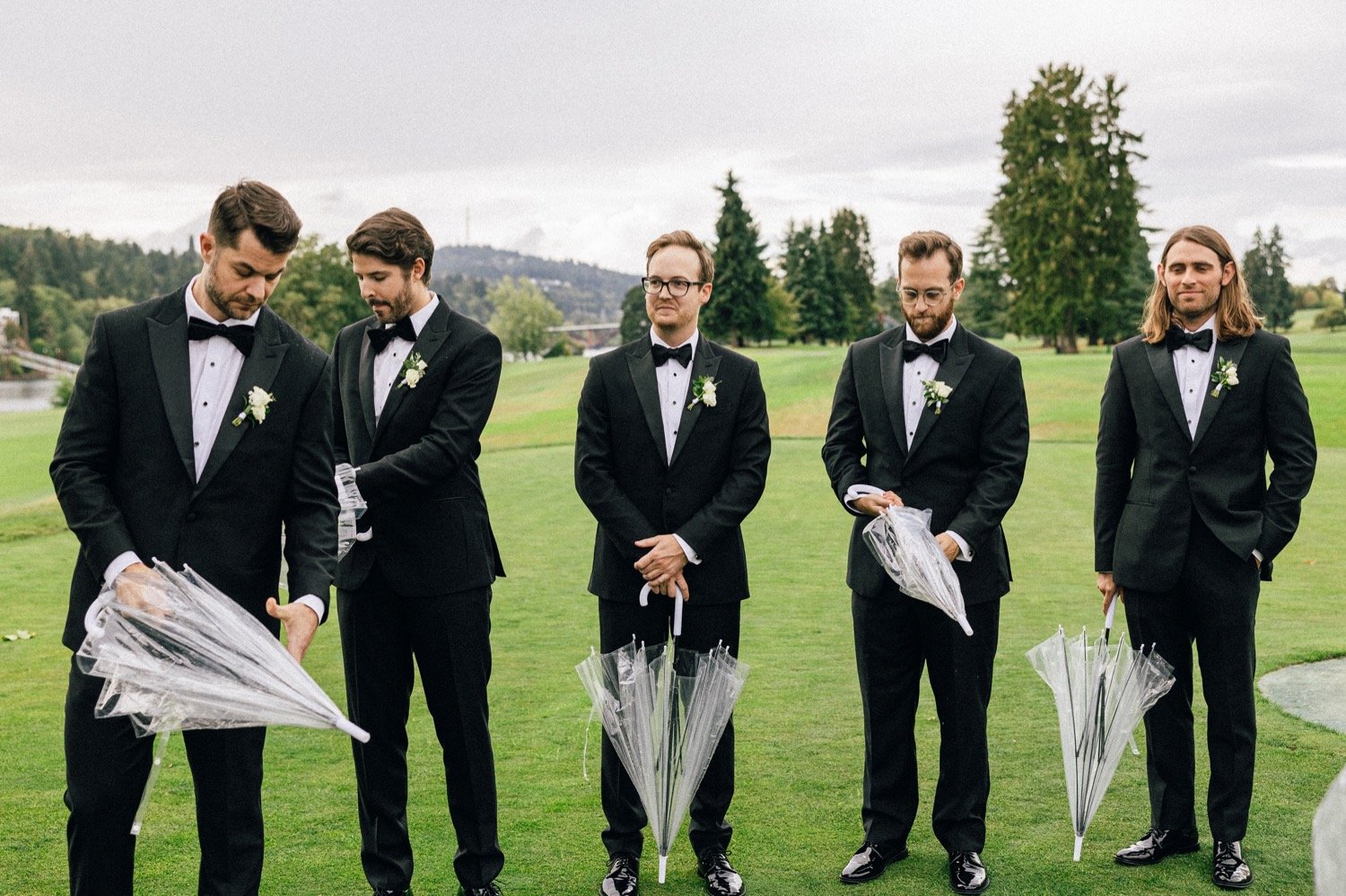  Five groomsmen in black suits hold clear umbrellas during wedding ceremony 