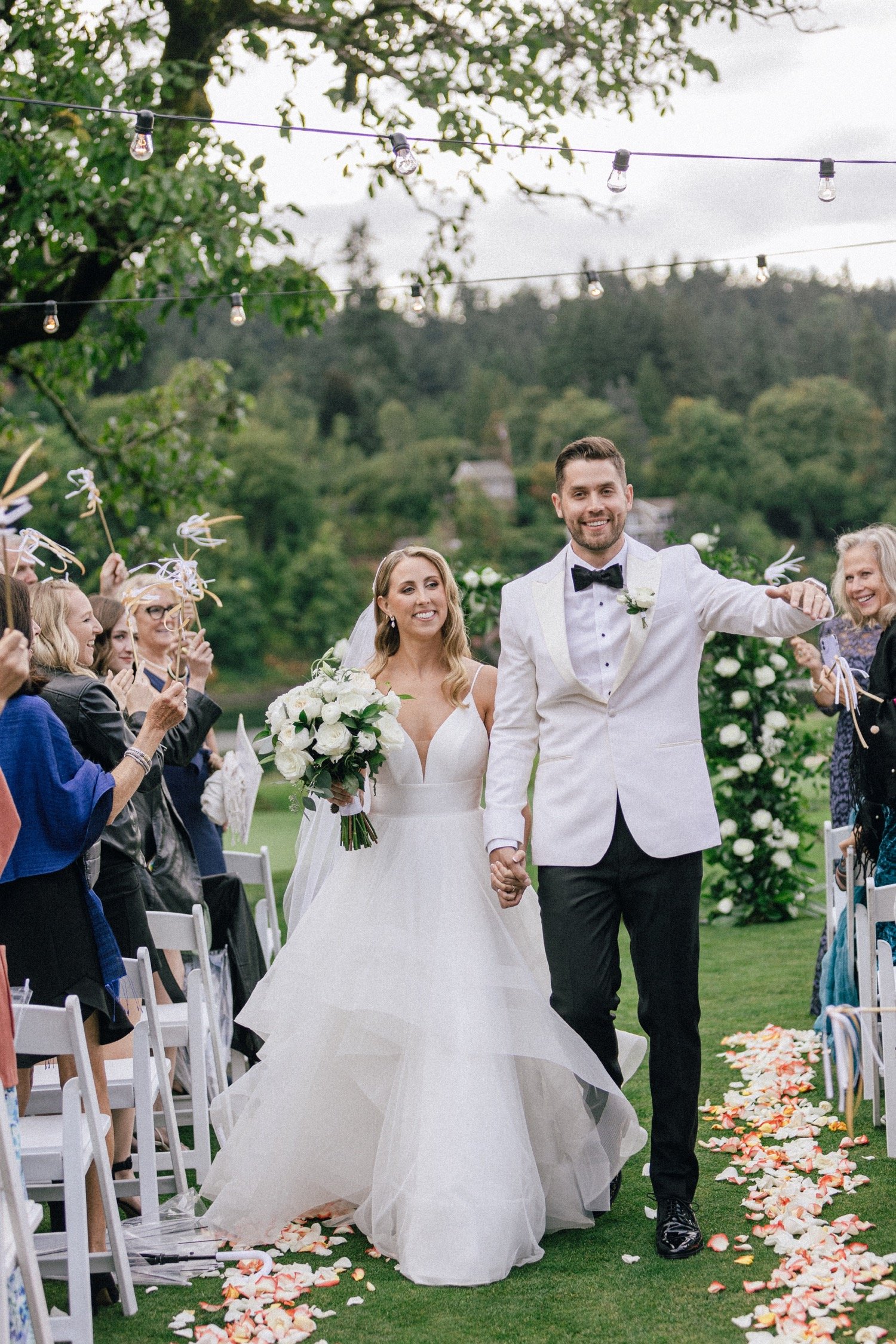  Bride in white dress and groom in white suit jacket and black pants exit wedding ceremony 