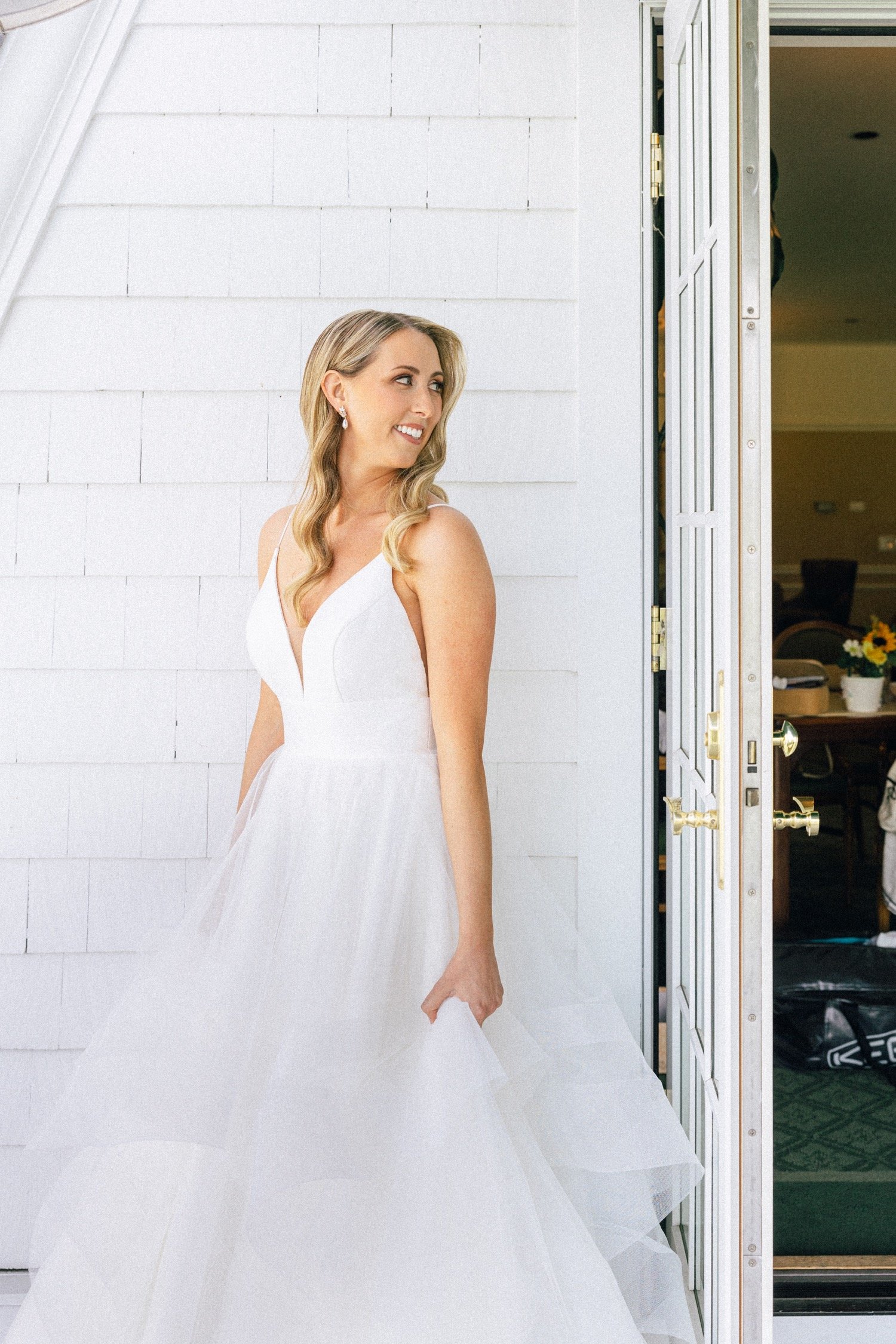  Bride in white dress looks over should while standing in front of white wall 