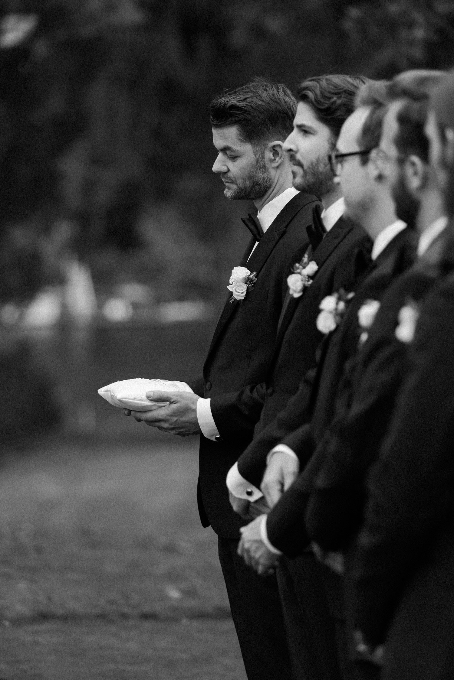  Groomsmen stand next to one another during wedding ceremony 
