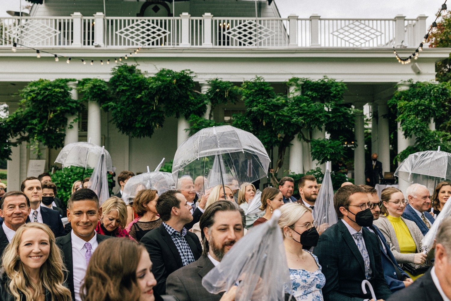  Wedding guests open clear umbrellas during ceremony 