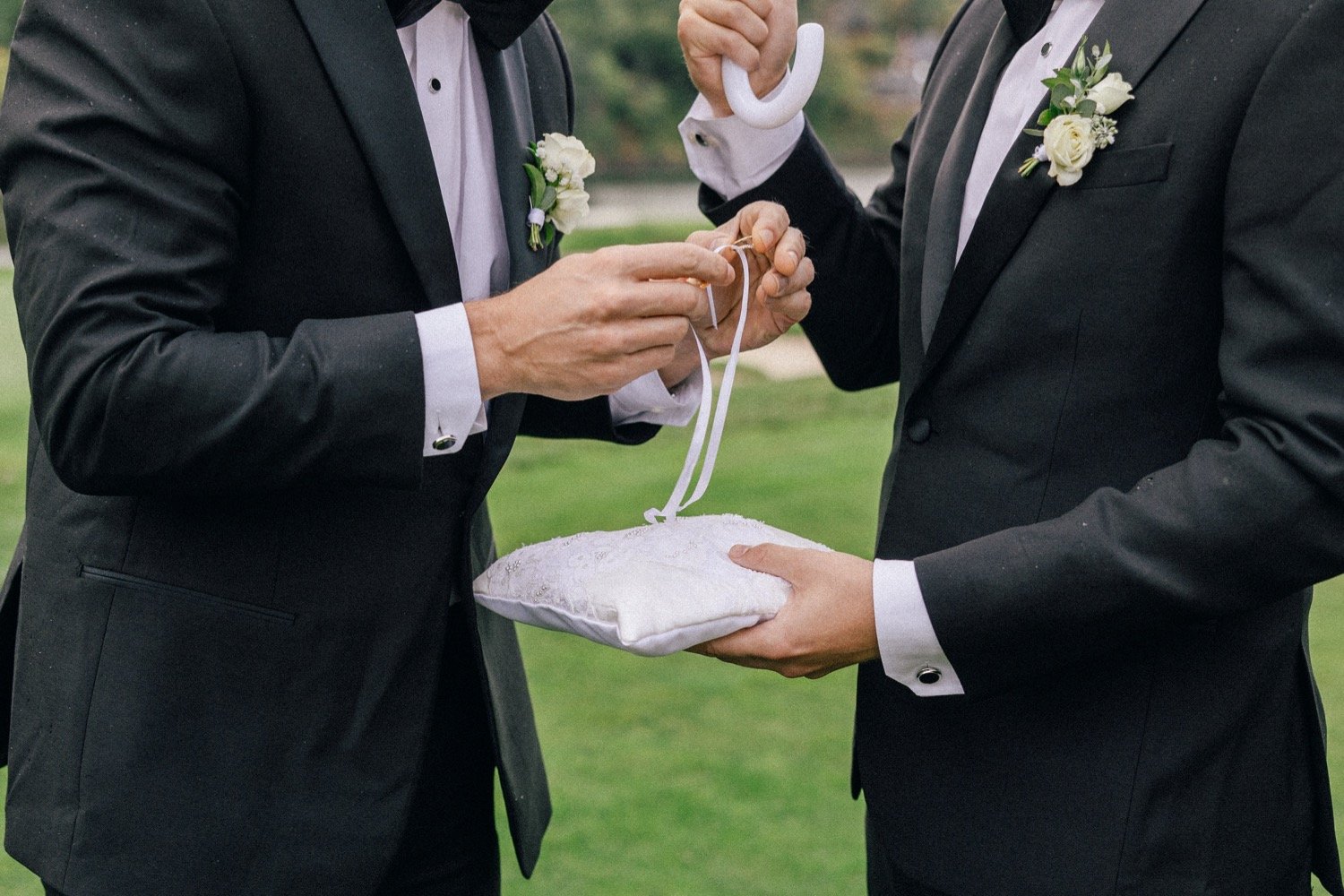  Man’s hands untie wedding bands from white pillow 
