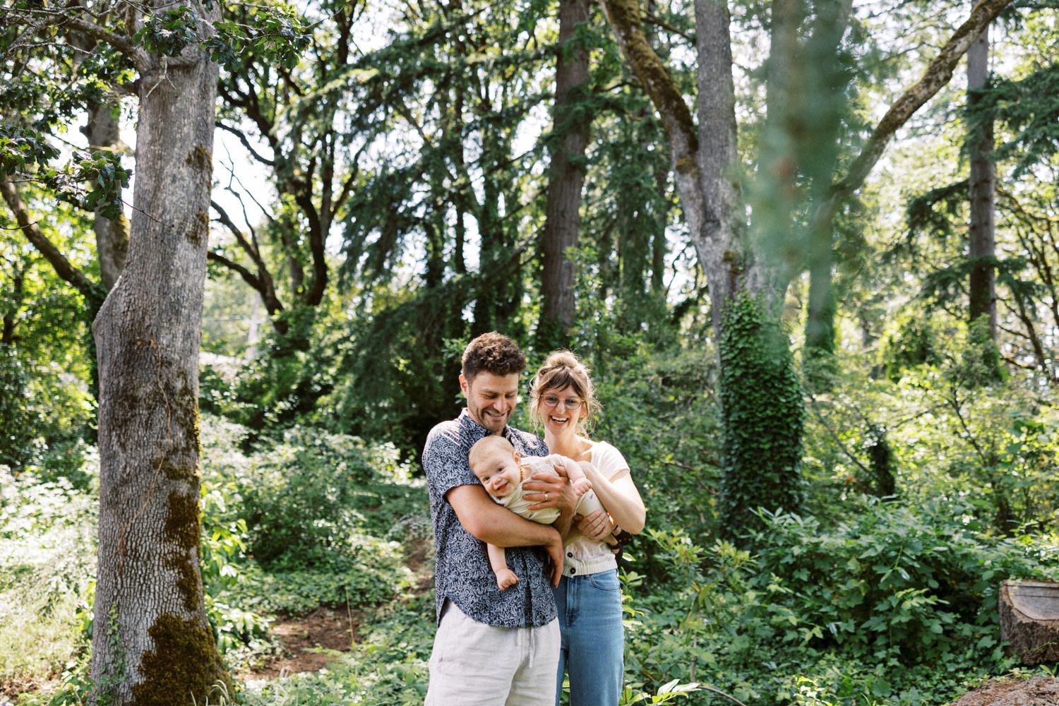 10_Portland Family Photographer-7579_mom and dad hold baby daugher while surrounded by trees and greenery.jpg