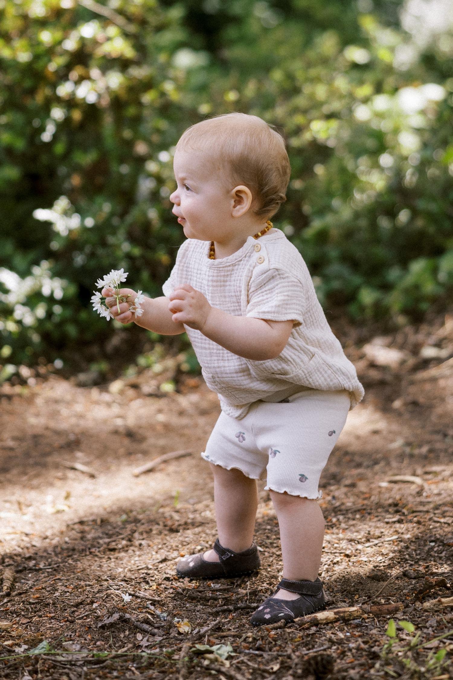 13_Portland Family Photographer-7368_baby girl holds white flowers while standing on dirt path.jpg