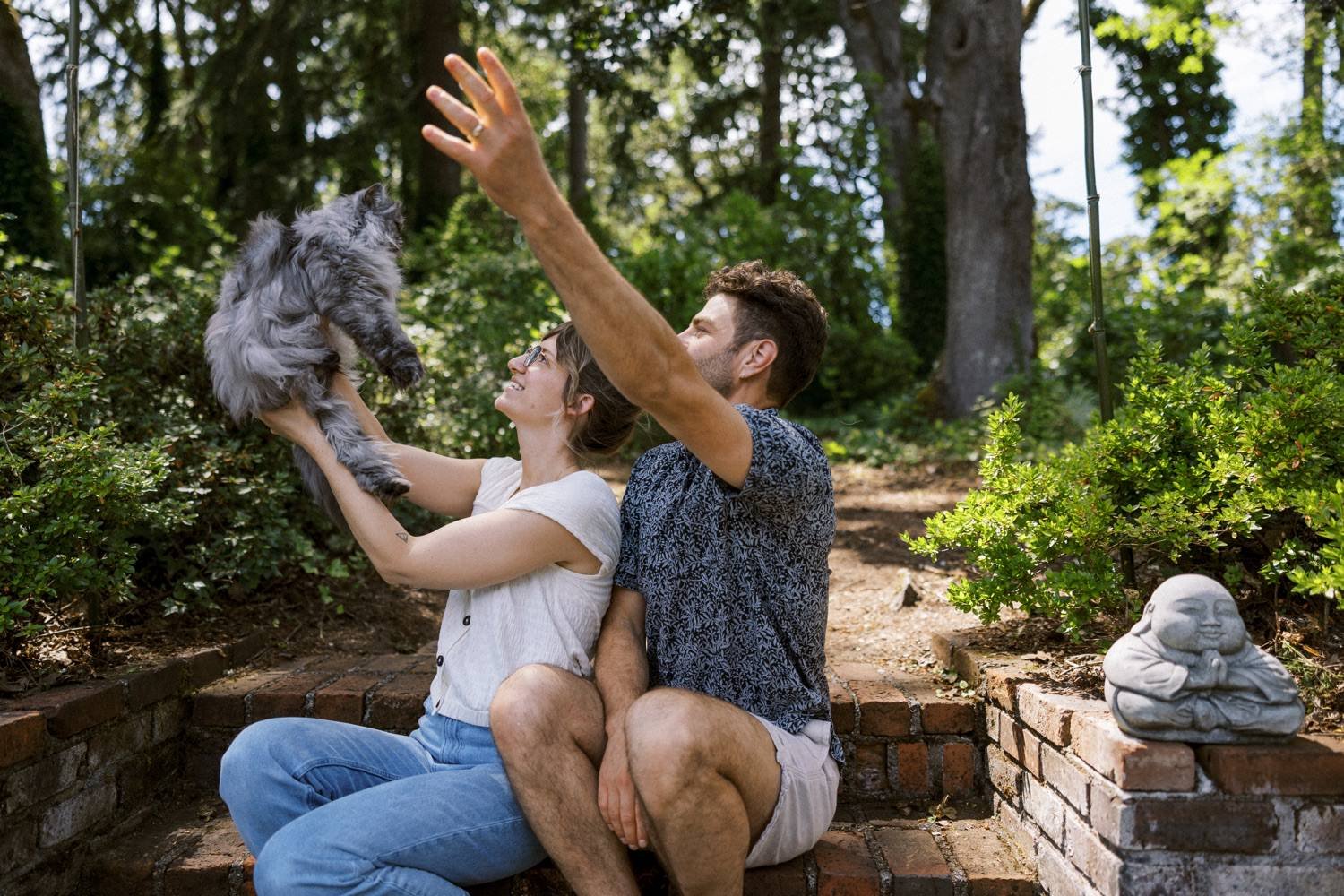 25_Portland Family Photographer-7896_man and woman hold up cat while sitting on brick steps in backyard.jpg