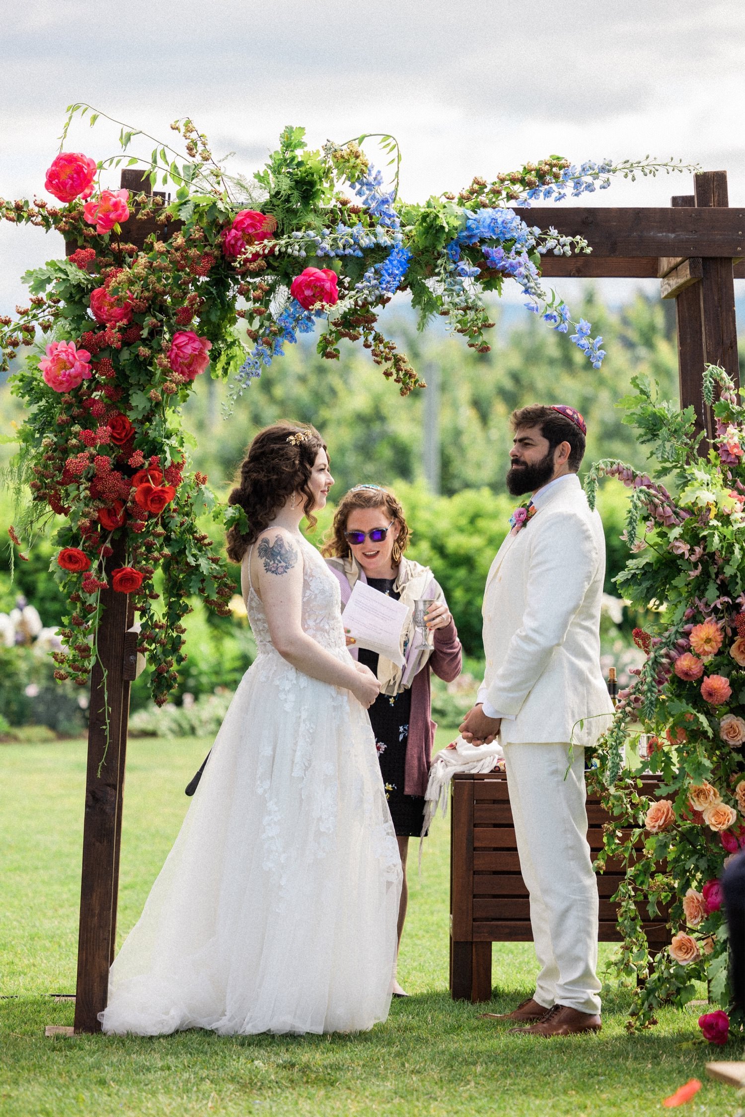 044_The Orchard Hood River Wedding2_bride and groom stand under floral arch during wedding ceremony.jpg