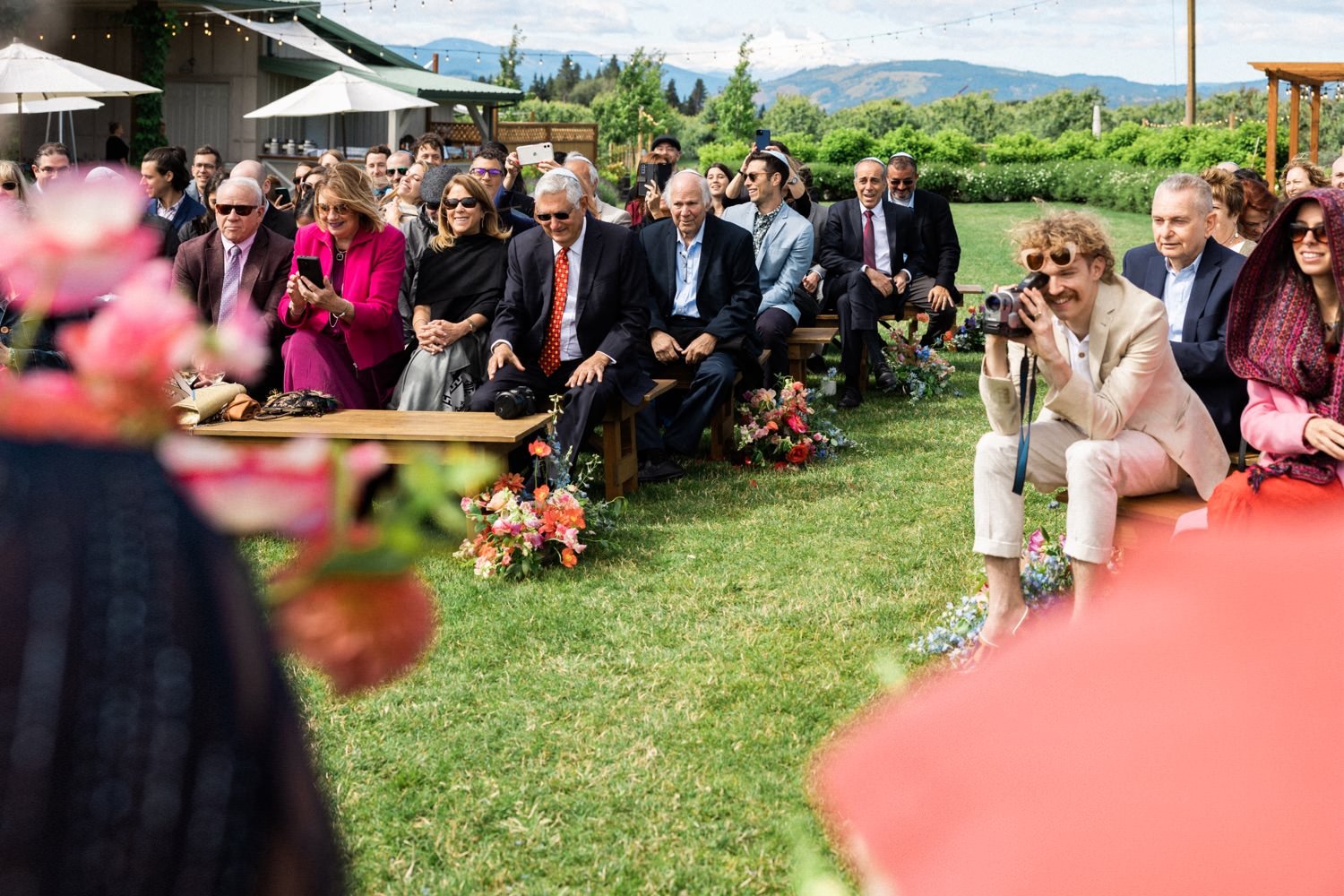 045_The Orchard Hood River Wedding90_wedding guests sit on wood benches and watch wedding ceremony.jpg