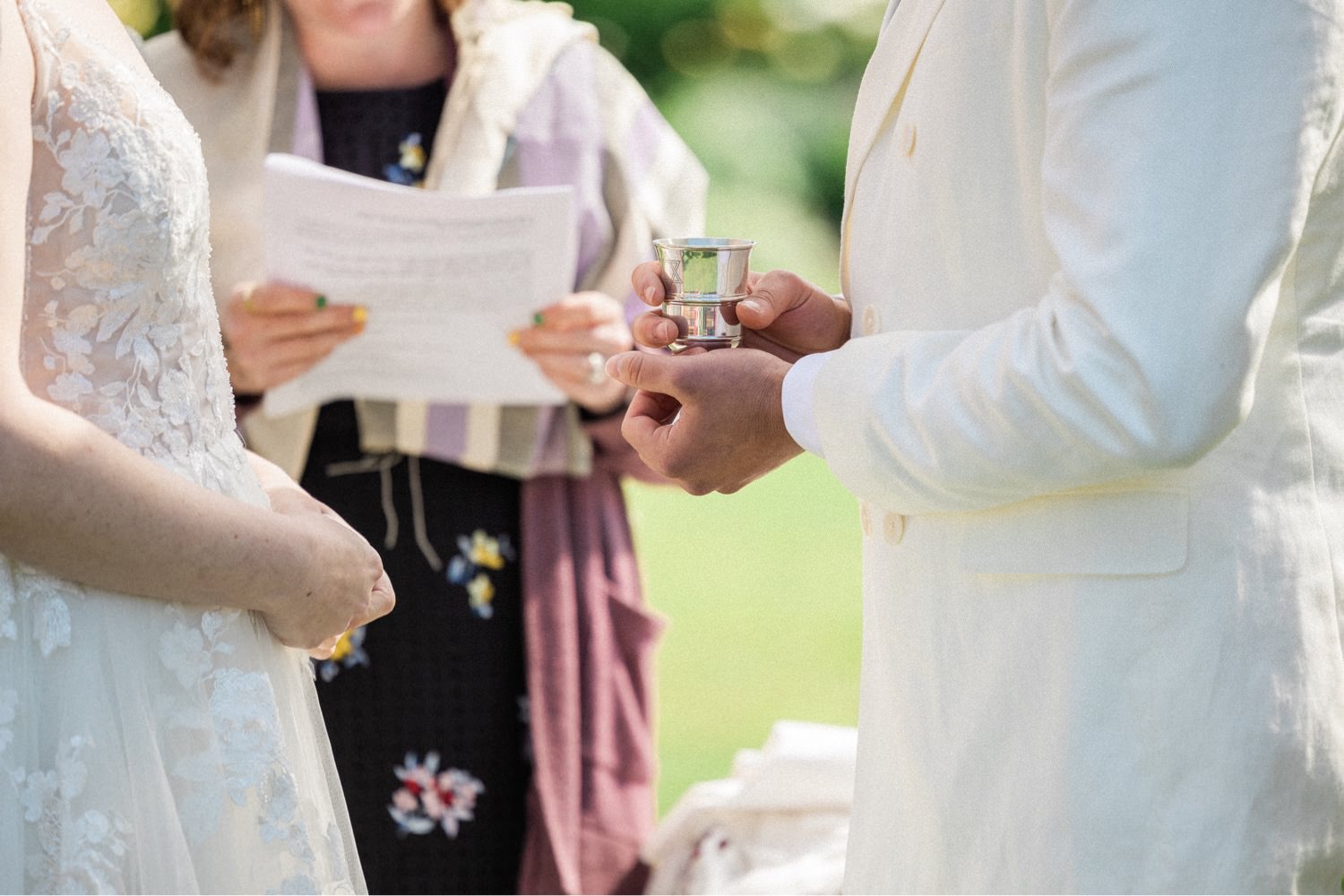 051_The Orchard Hood River Wedding8_groom in white suit holds small silver cup in hands during wedding ceremony.jpg