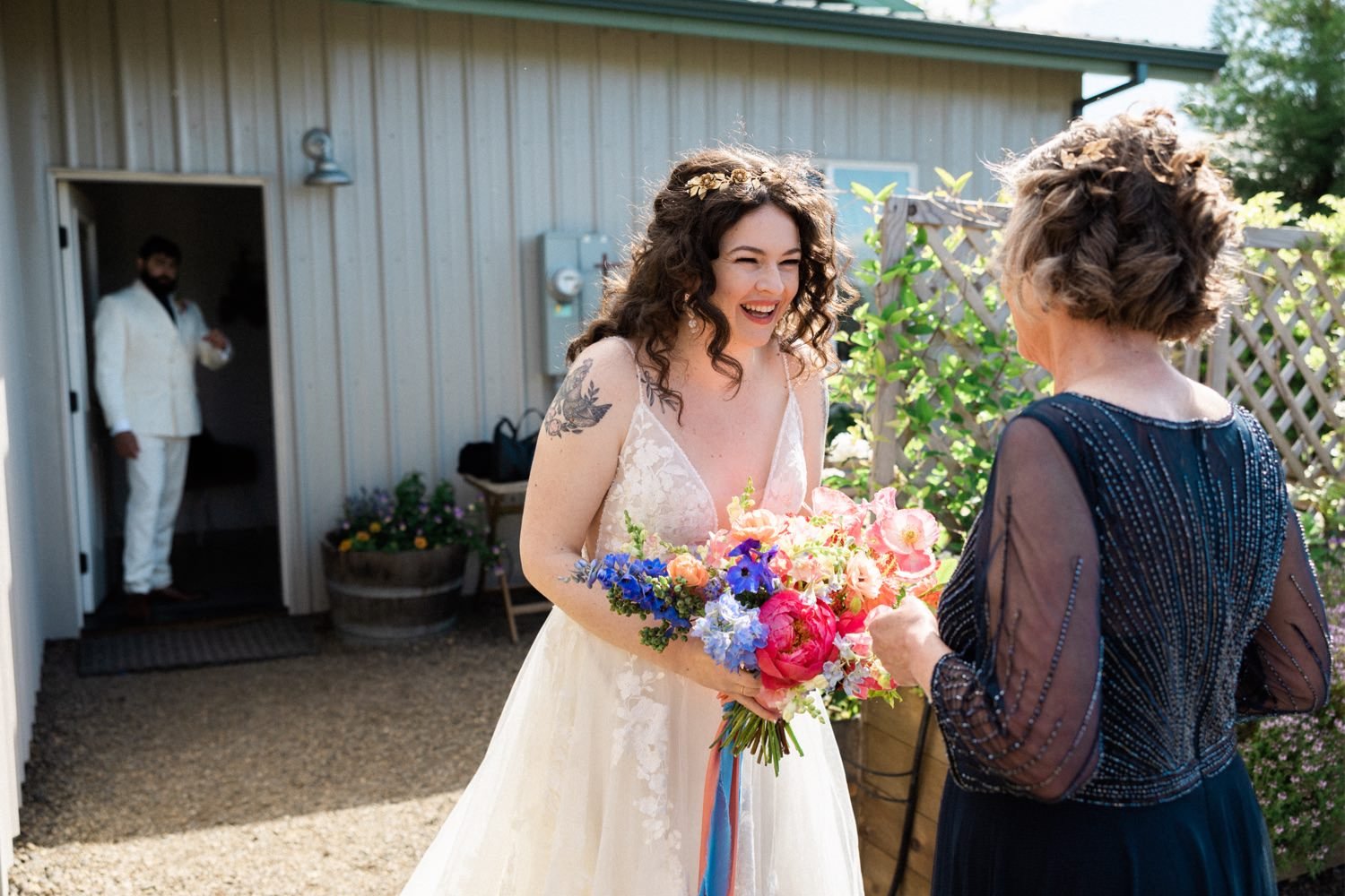 063_The Orchard Hood River Wedding105_bride smiles at mom whiel holding bouquet of colorful flowers.jpg