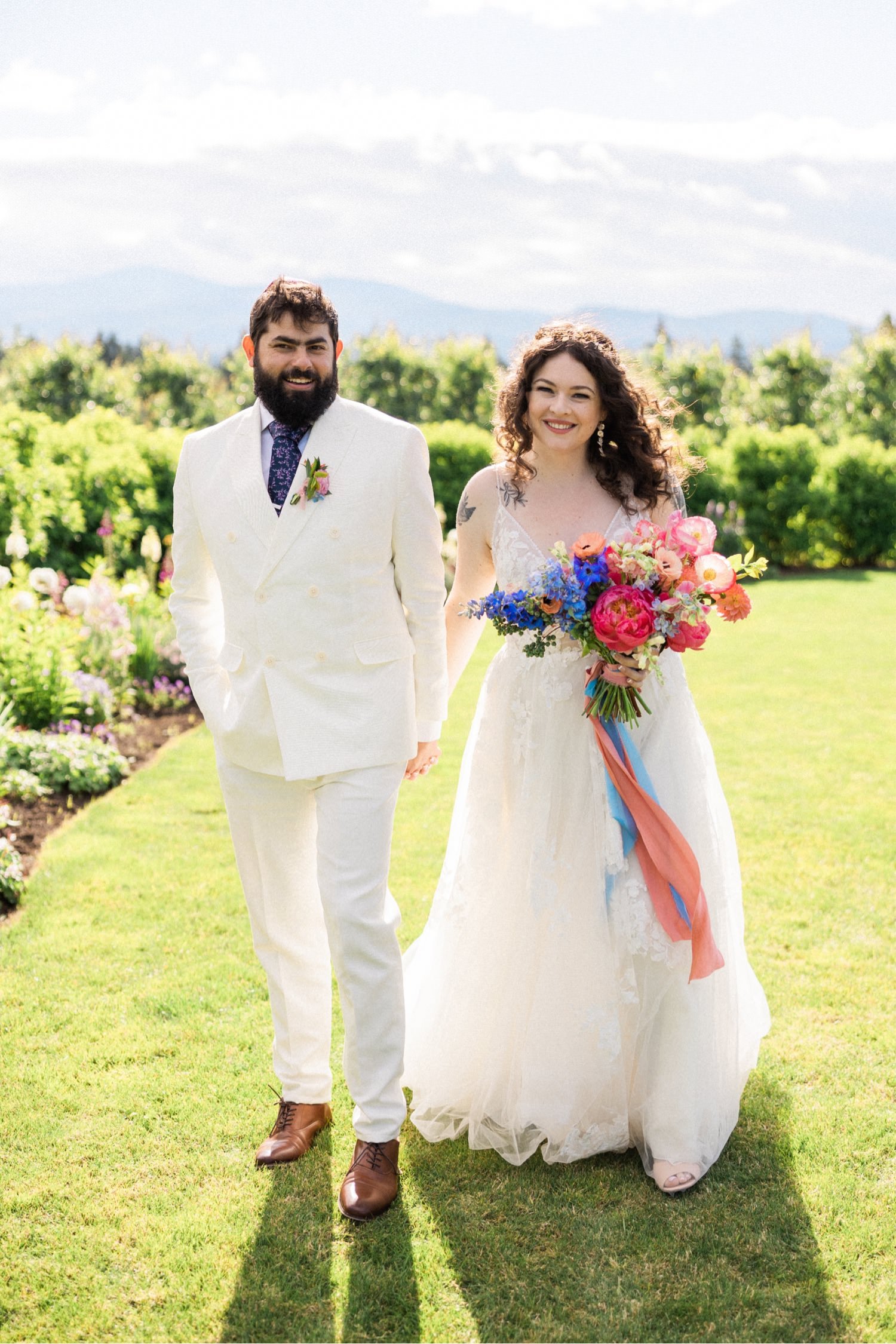 074_The Orchard Hood River Wedding116_bride in white dress holding bouquet of purple and pink flowers holds hand of groom in white suit and kippah.jpg