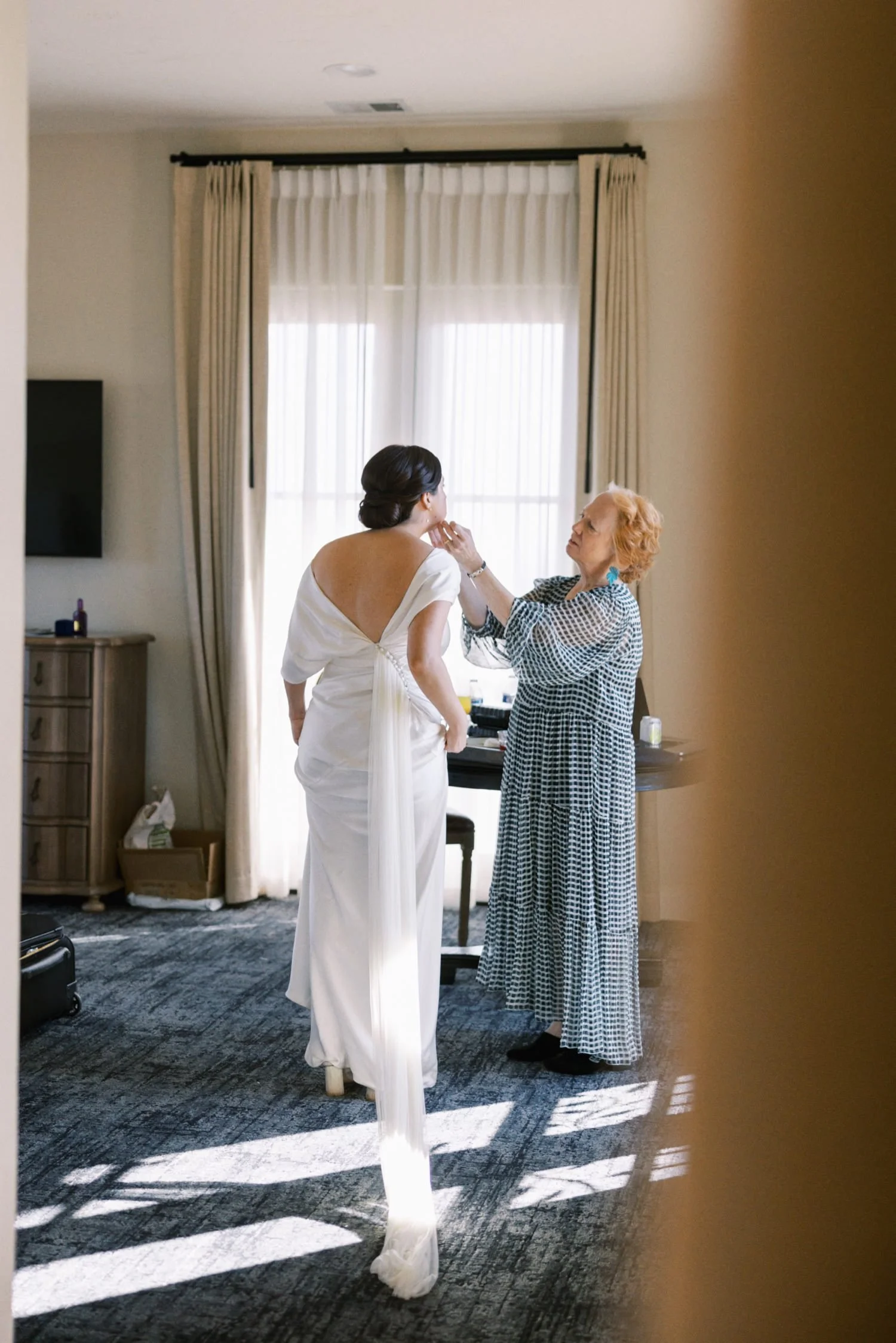  mother of the bride in checkered black and white dress holds the face of bride in white wedding gown 