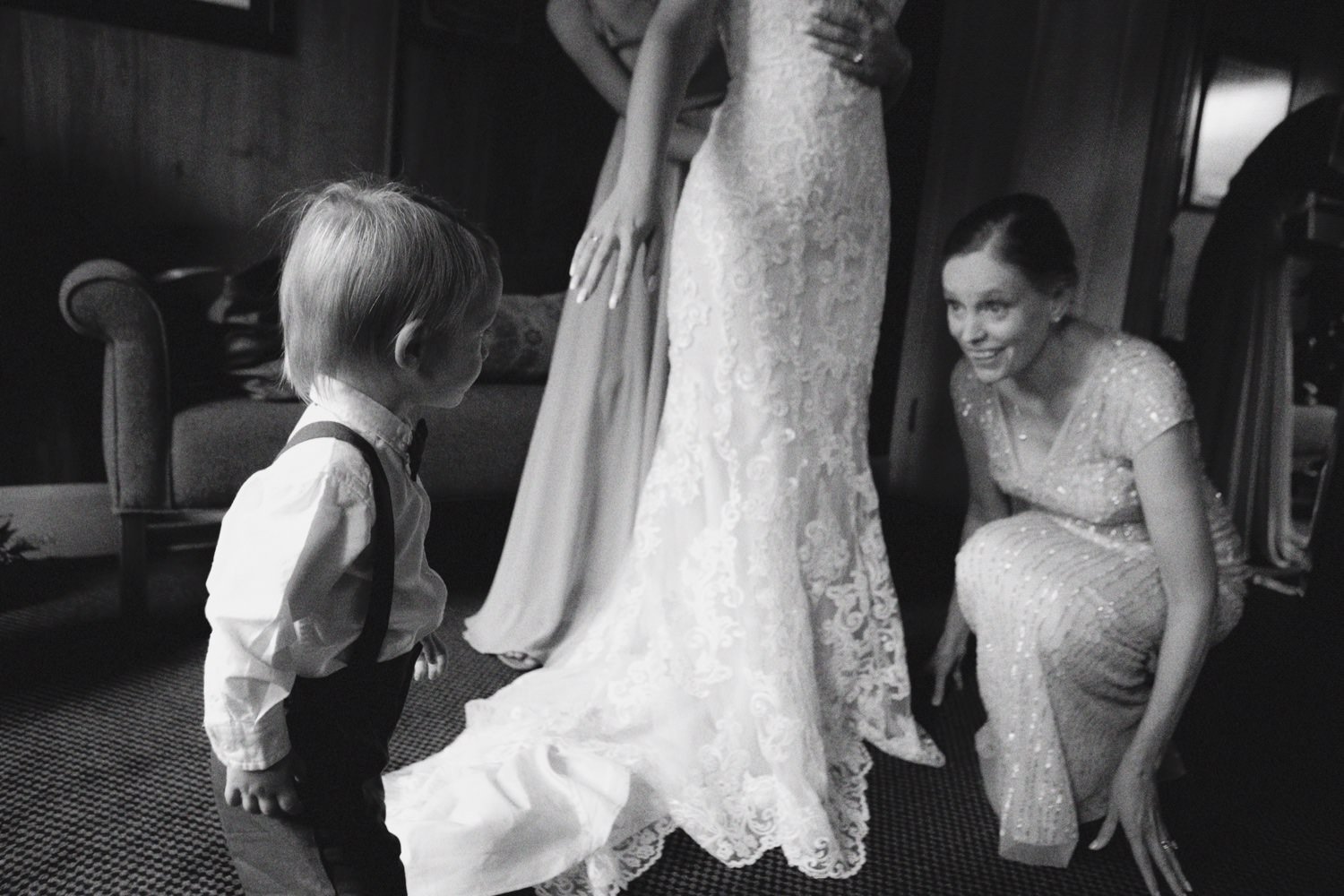  toddler boy stands in front of bride getting into dress 