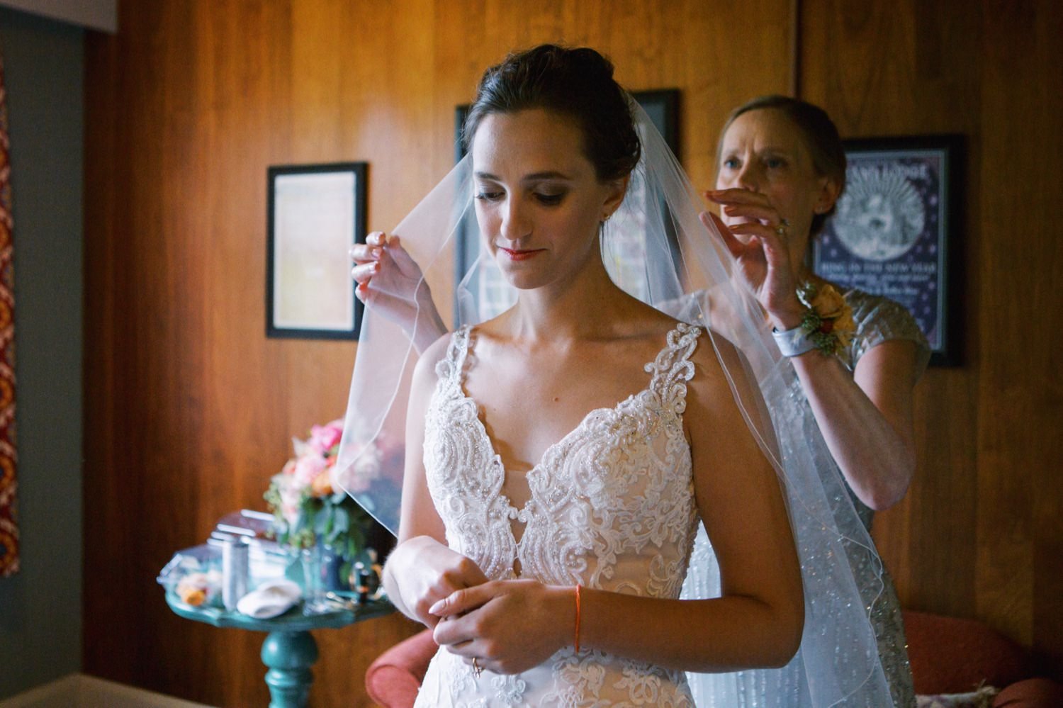  mother of the bride places veil on woman wearing wedding dress 
