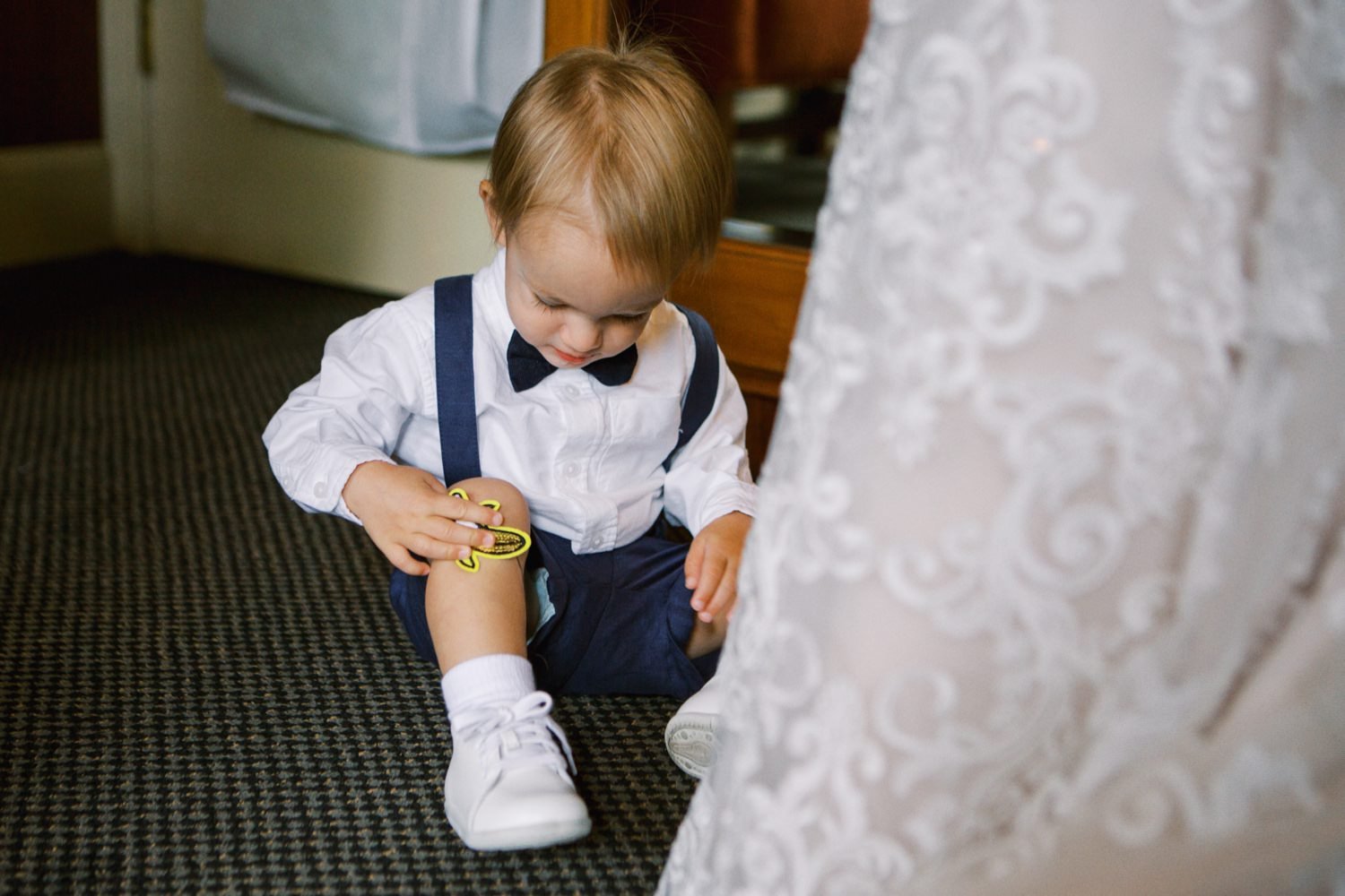  toddler in suspenders and bowtie puts a banana sticker on his knee 