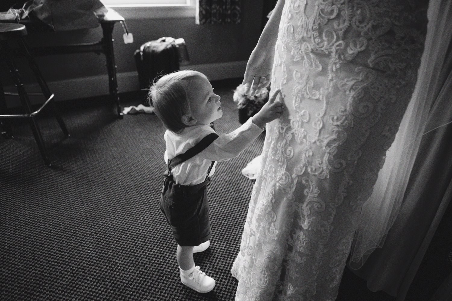  toddler in suspenders and bowtie points at wedding dress worn by bride 