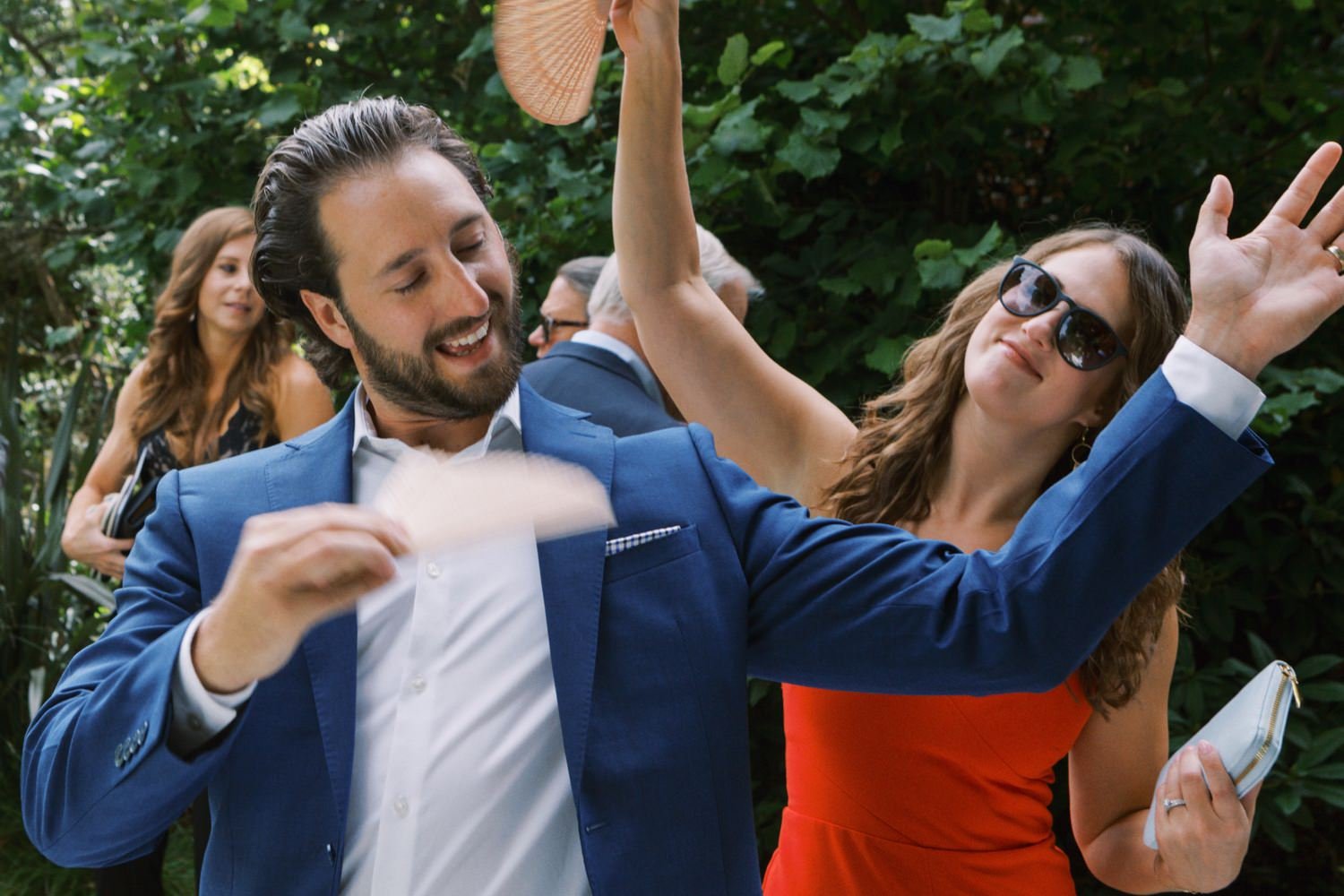  man in blue suit and woman in red dress fan themselves with mini hand fans 