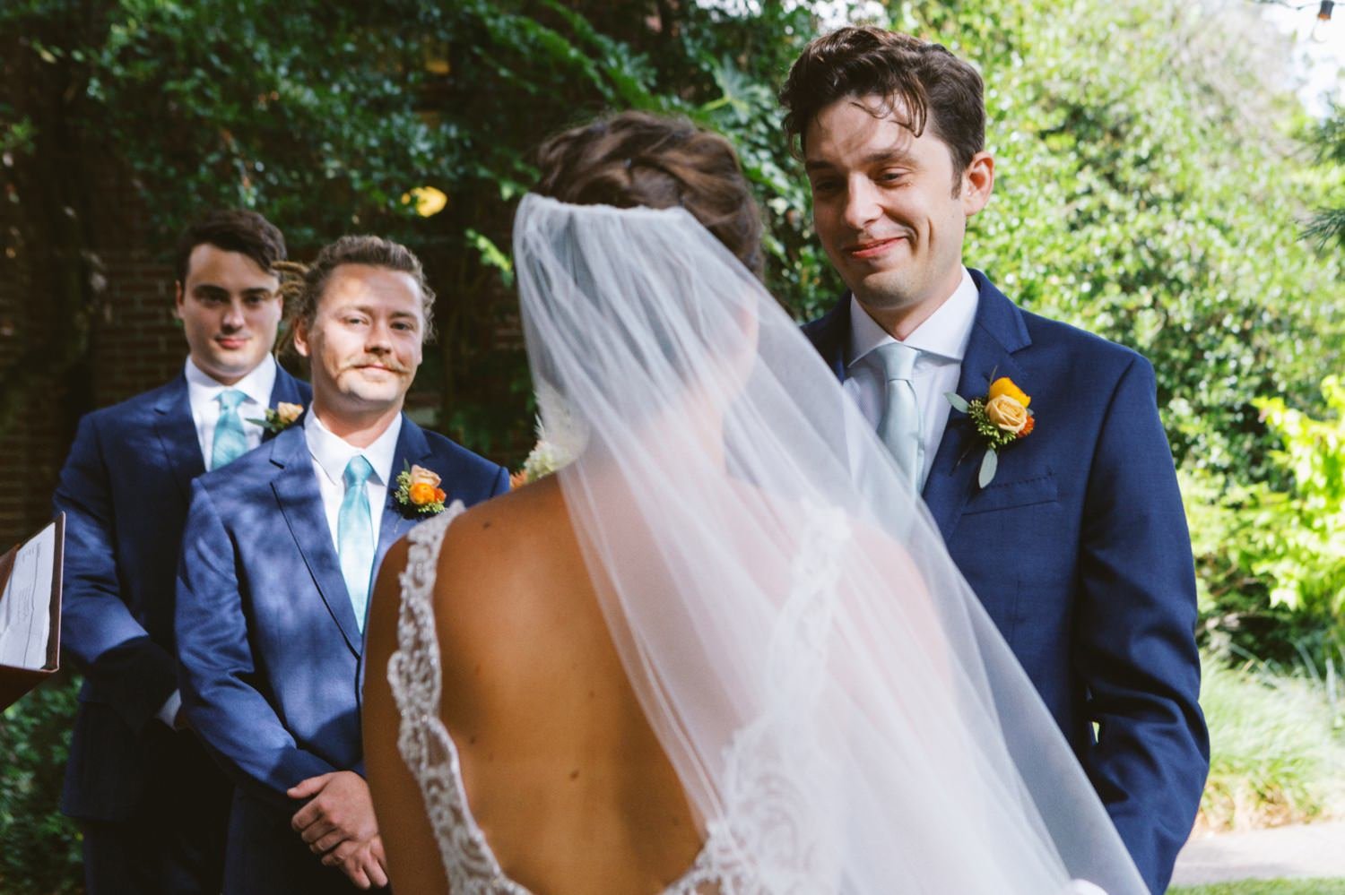  groom in blue suit smiles at bride in white dress and veil 