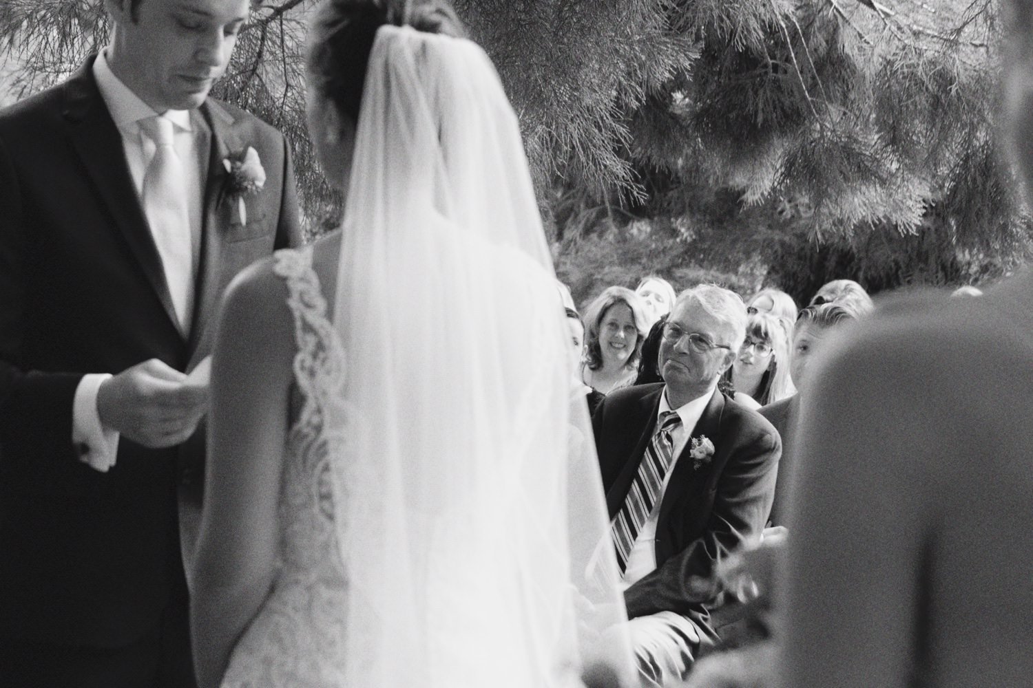  father of the bride looks at bride and groom as groom reads vows to bride 