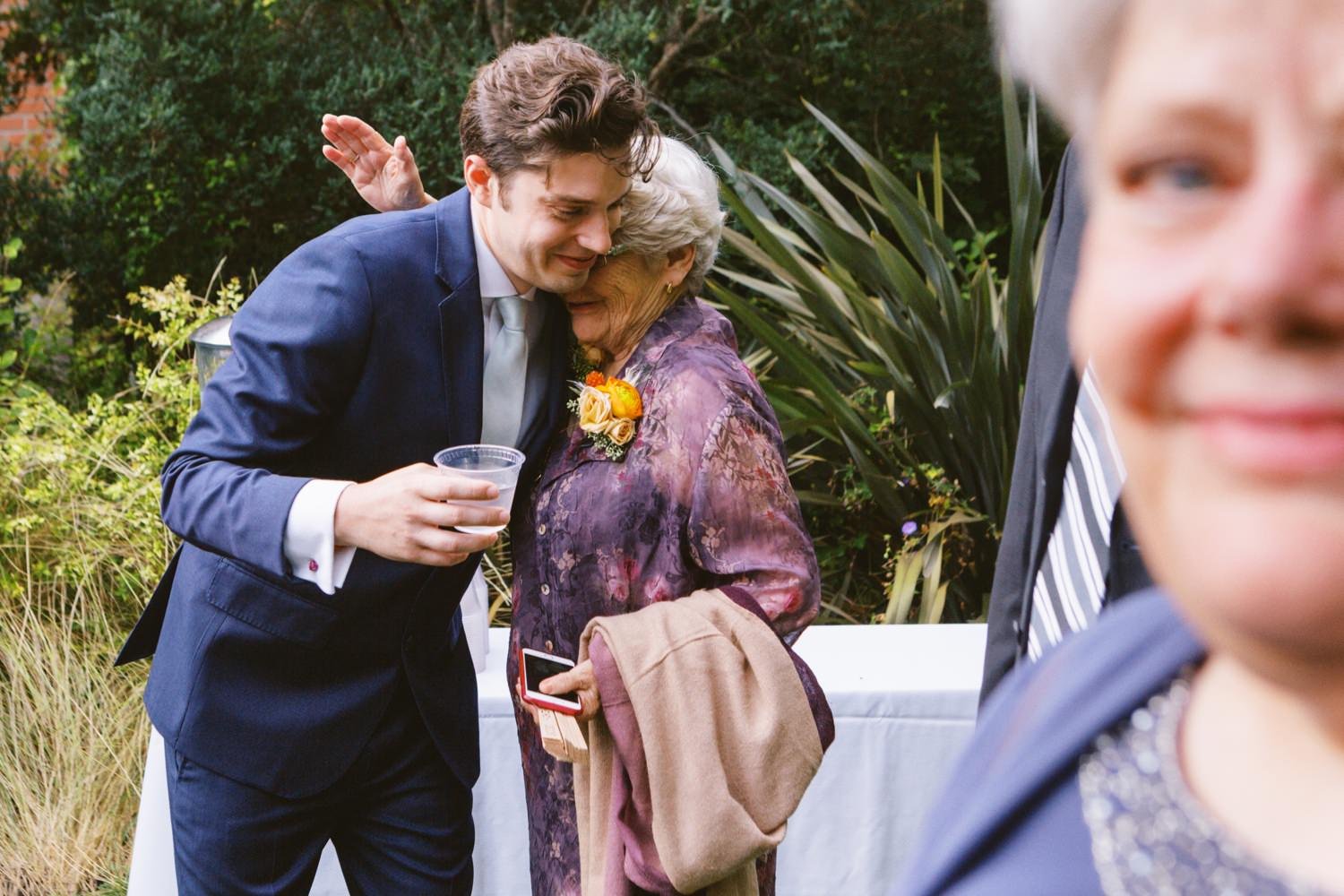  many holding glass of water wearing navy blue suit hugs grandmother in purple dress 