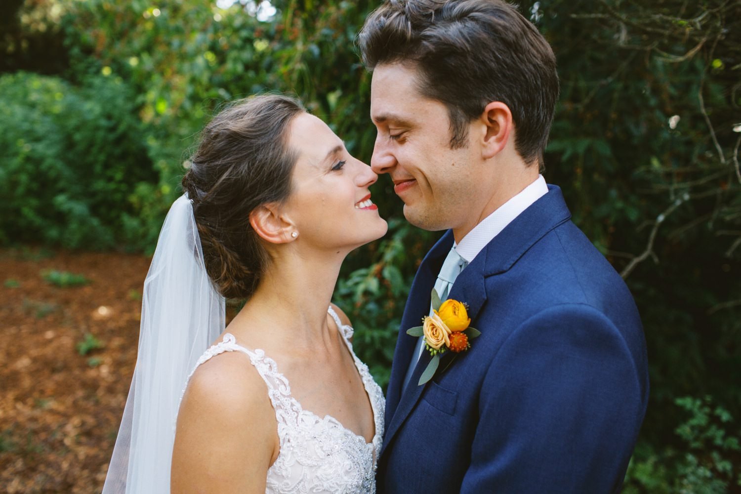  bride in white dress touches nose to nose of groom in navy blue suit 