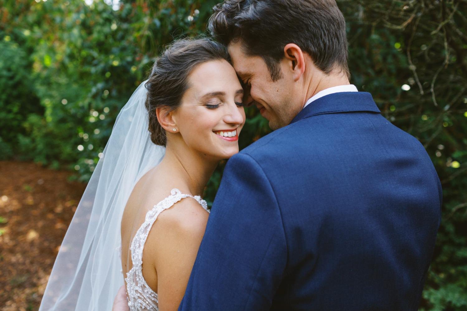  bride in white dress and groom in navy blue suit huge each other 