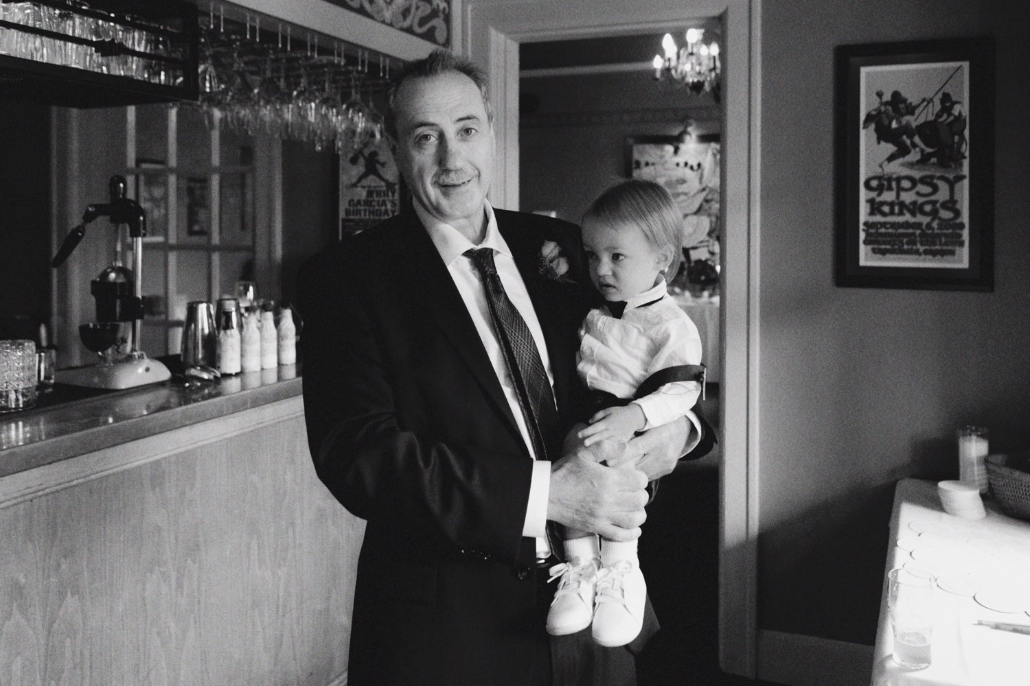  man in suit holds toddler in suspenders an white sneakers 