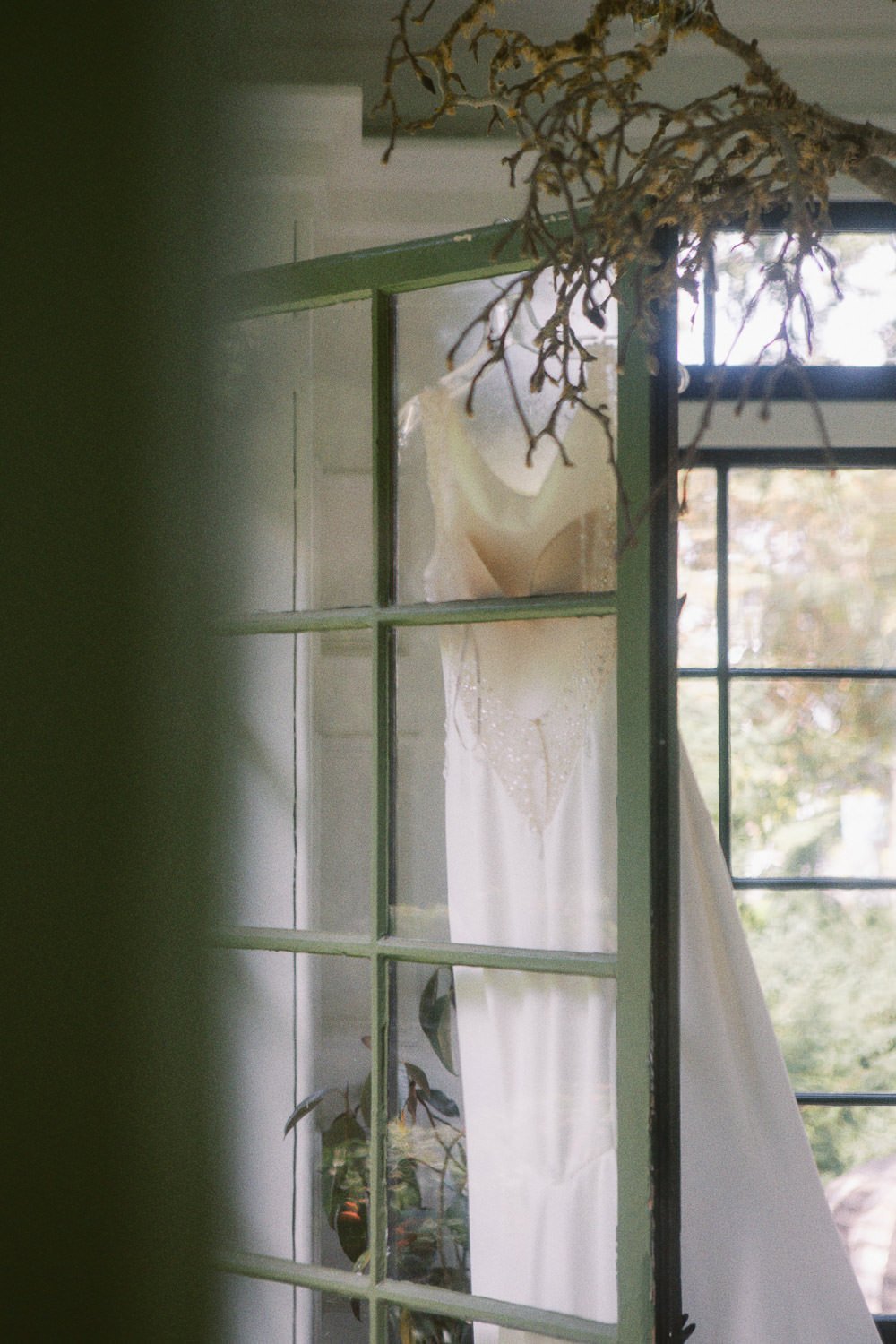  wedding dress hangs from green door frame at Deepwood Museum and Gardens wedding venue in Salem, Oregon 