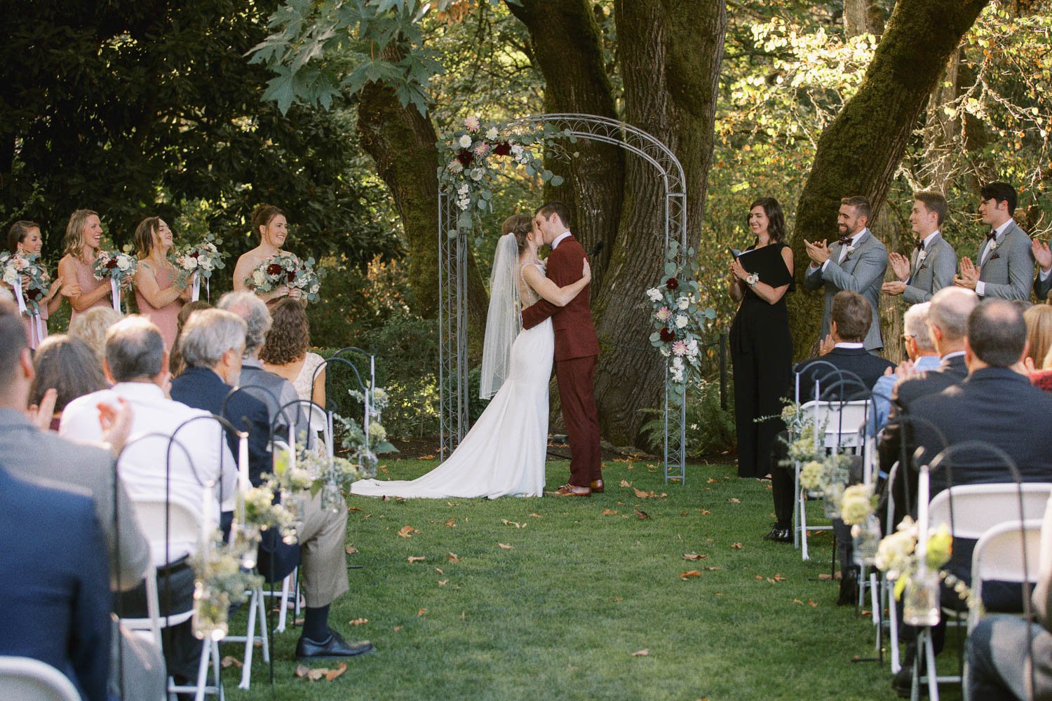  bride in white dress and groom in maroon suit share first kiss after wedding ceremony at Deepwood Museum and Gardens 