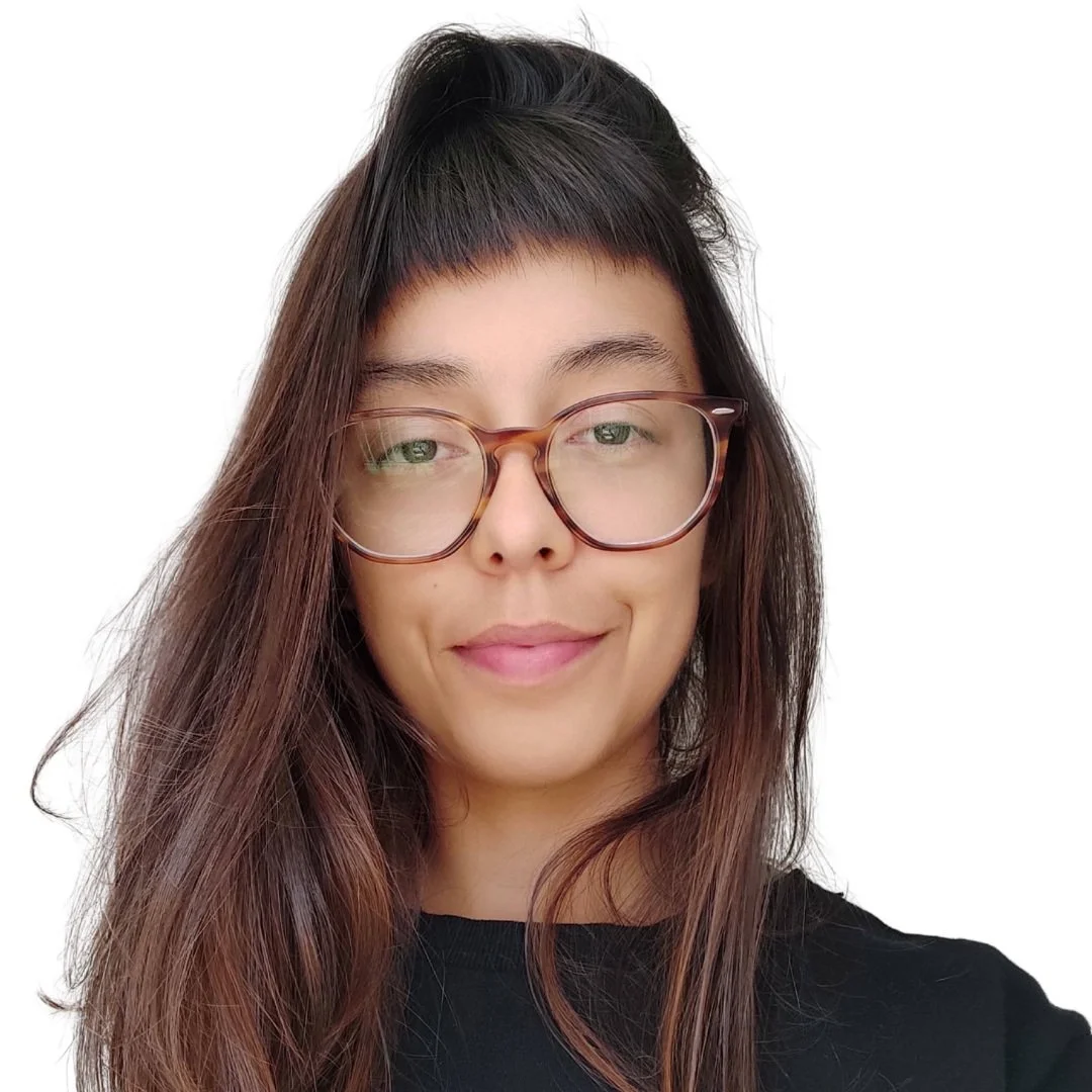 Retrato de uma mulher com cabelo castanho, usando óculos de armação grossa, com camisa preta, sorrindo, contra fundo branco.