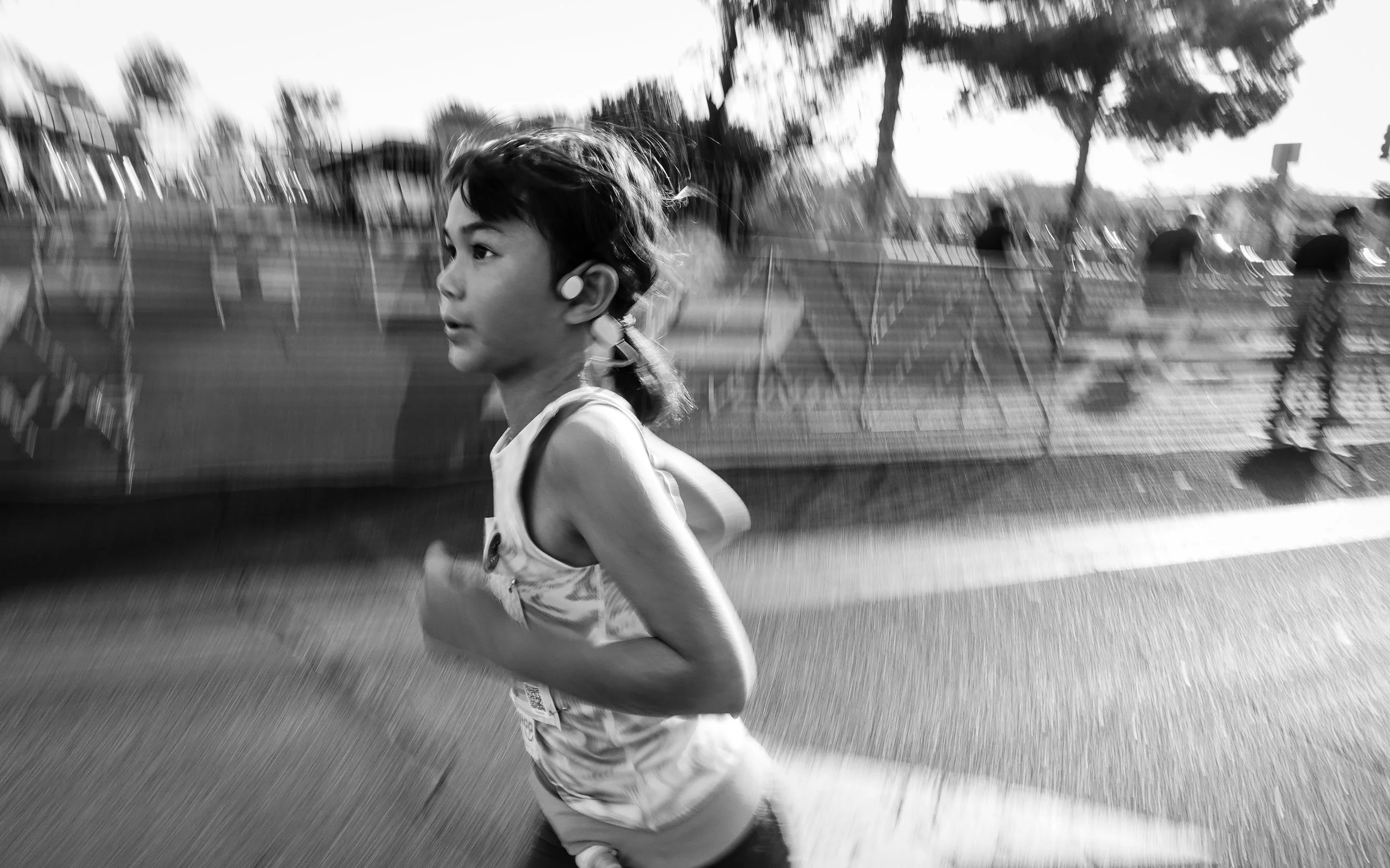 A black and white image of a girl running in a 5K race towards the finishing line with focused look on her face and motion blur in the background. Photographed by Phoenix Documentary Family Photographer Amy Dangerfield.