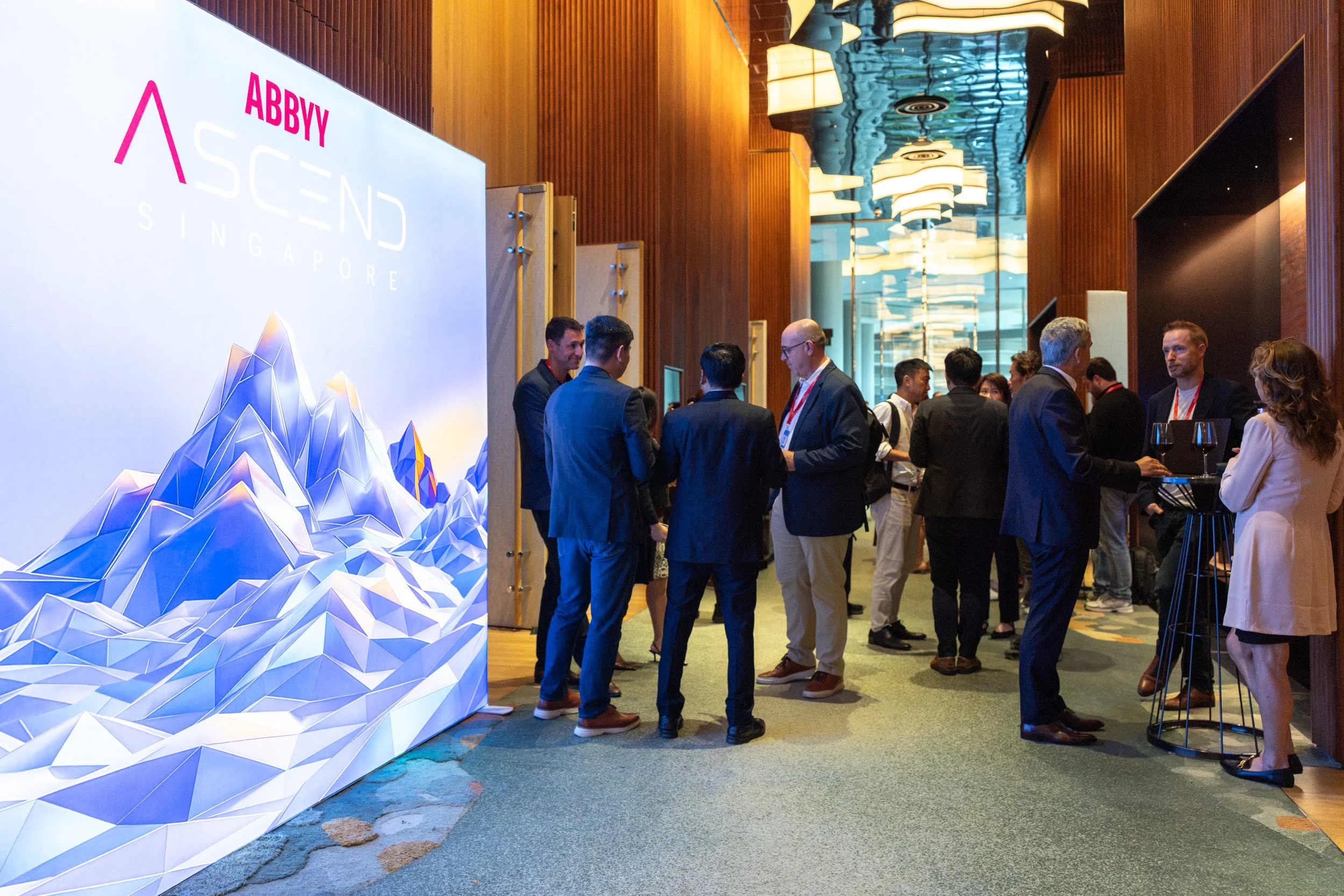  Attendees networking in front of a branded ABBYY photo backdrop wall at a Singapore corporate event. 