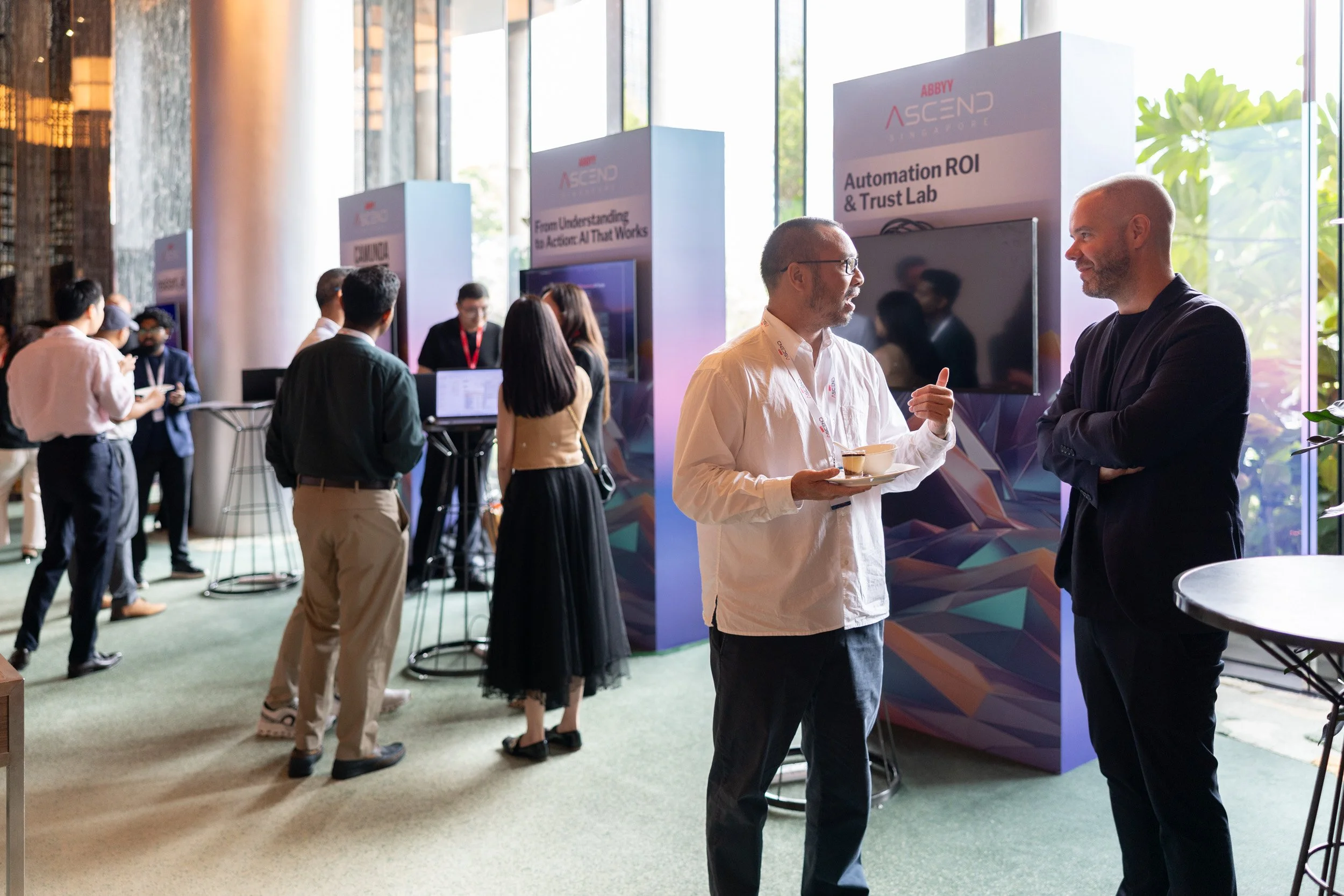  Corporate event attendees networking near partner exhibition booths outside the seminar hall. 