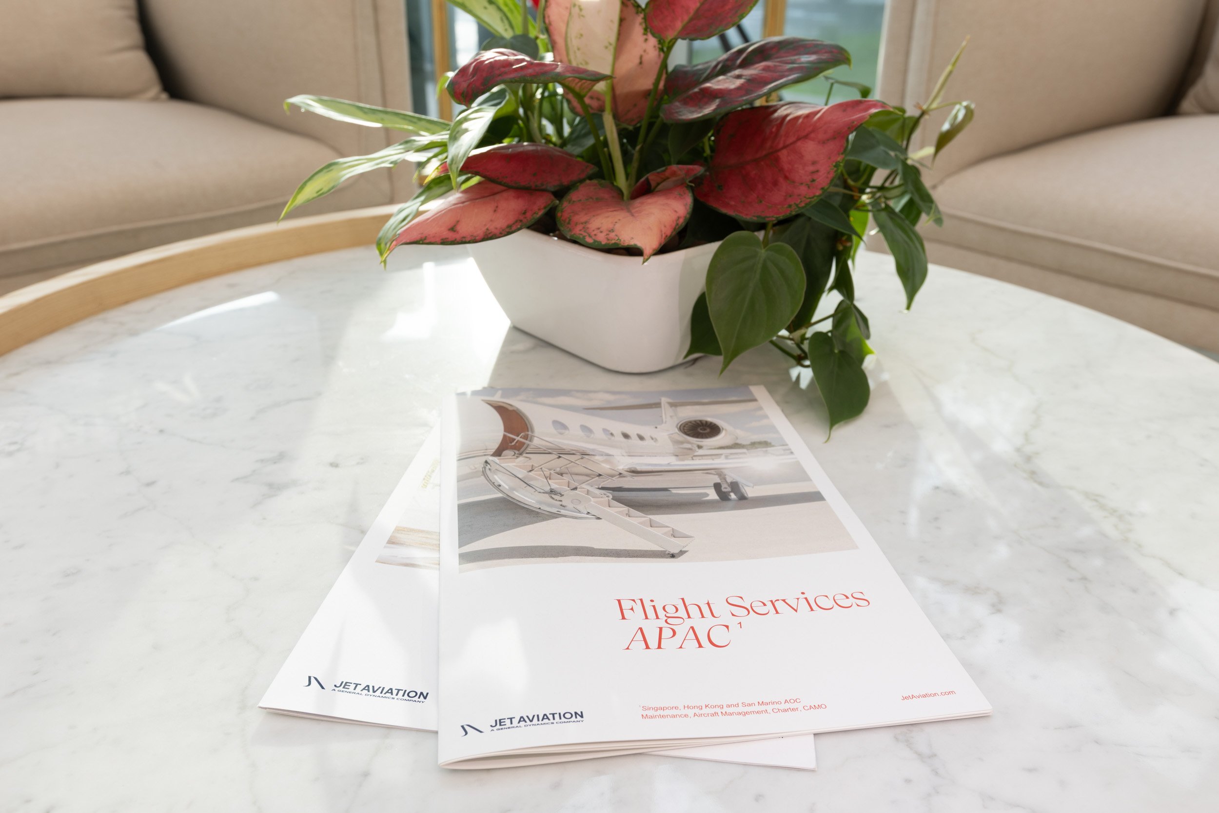  Jet Aviation branded corporate brochures and floral arrangement displayed on a VIP lounge coffee table. 
