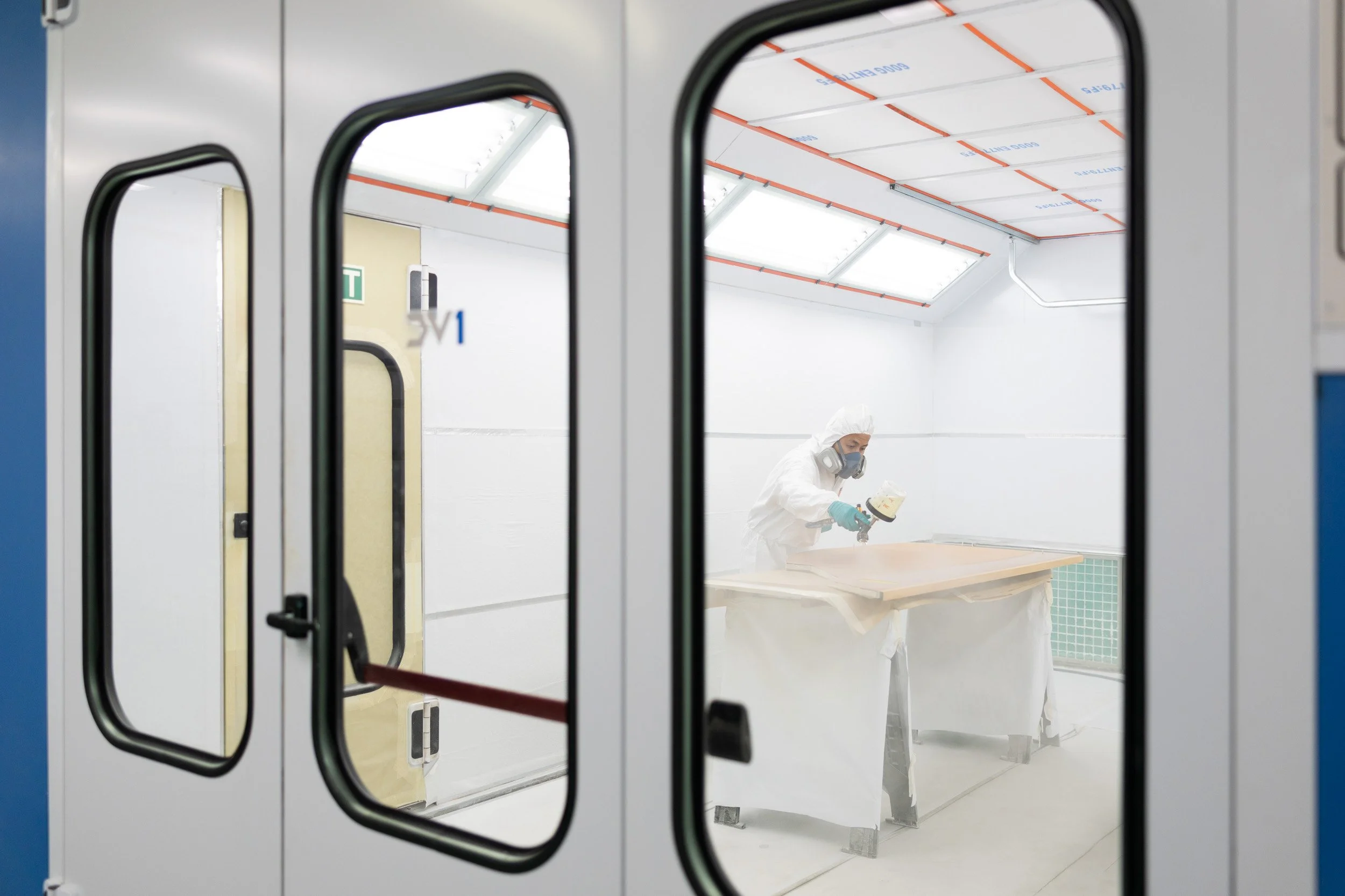 Wide perspective through viewing glass of technician in protective suit applying specialized aircraft coating. 
