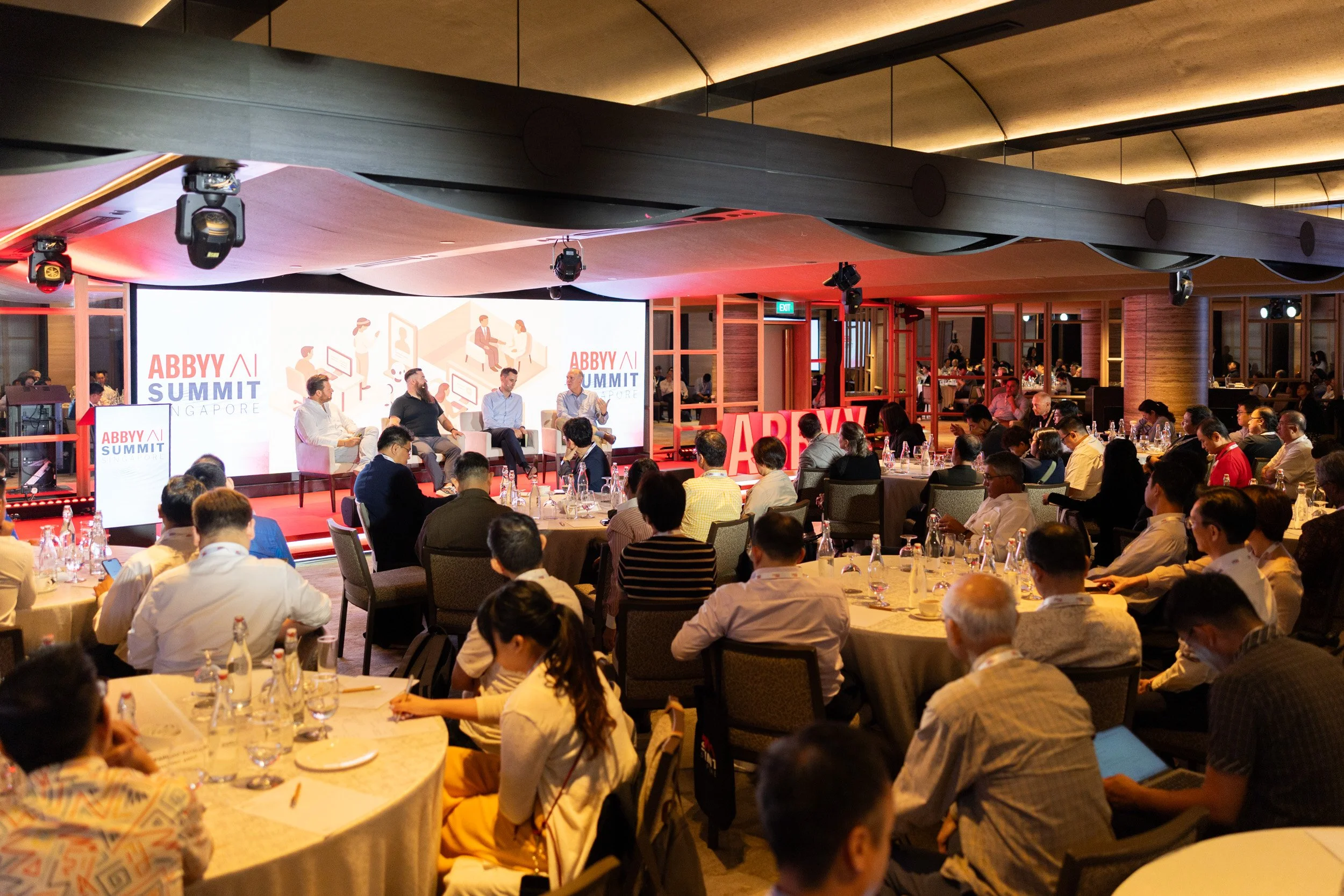  Wide angle auditorium shot showing seated event attendees watching the executive panel session on stage. 