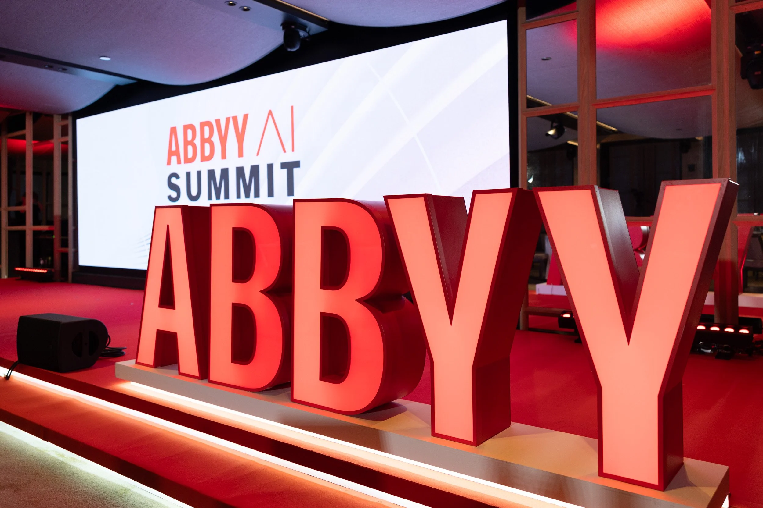  Physical ABBYY logo on stage in front of a large screen displaying the AI Summit Singapore event title at PARKROYAL COLLECTION Marina Bay. 