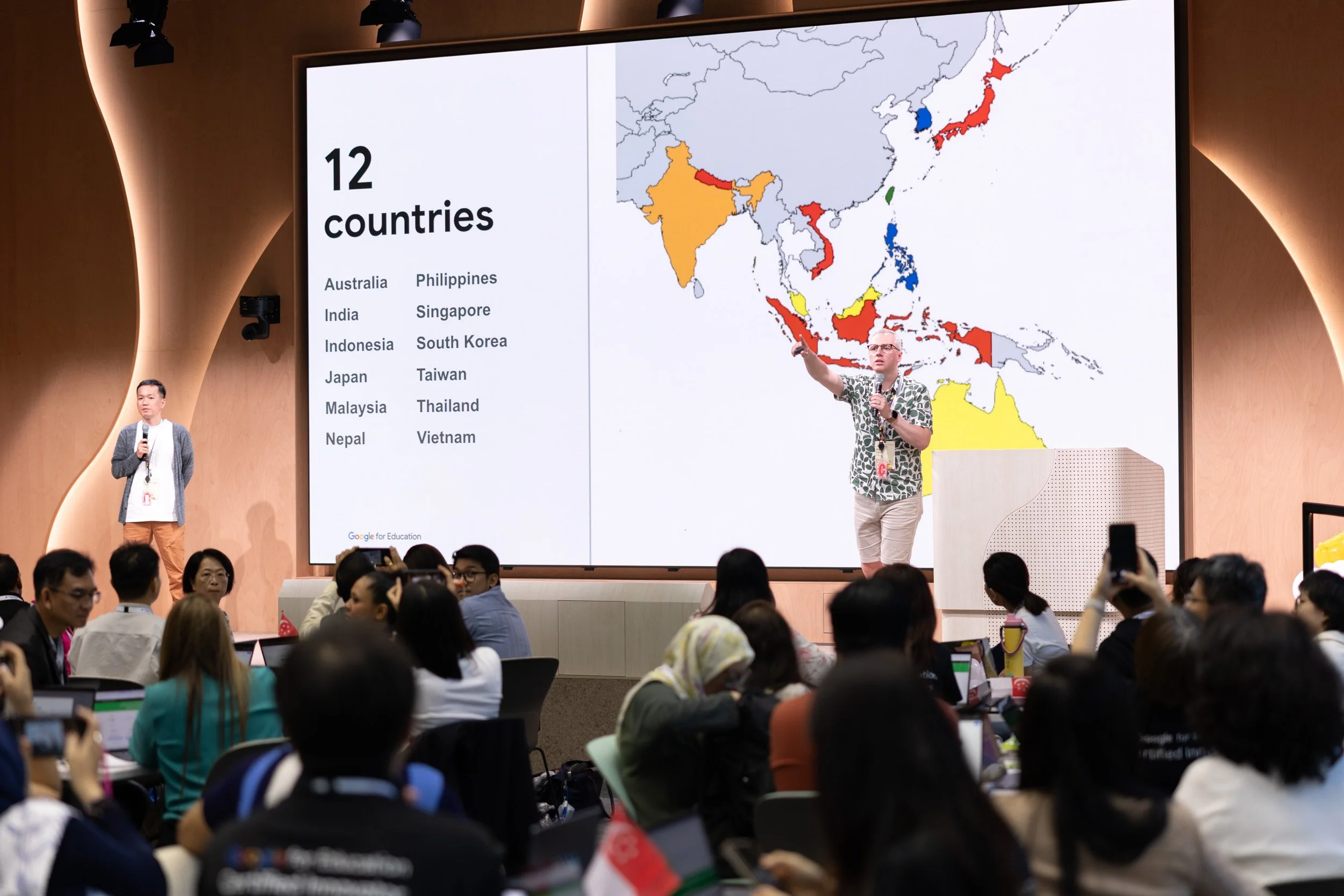  Medium photograph of speaker Phil Carew presenting on stage during the Google symposium. 