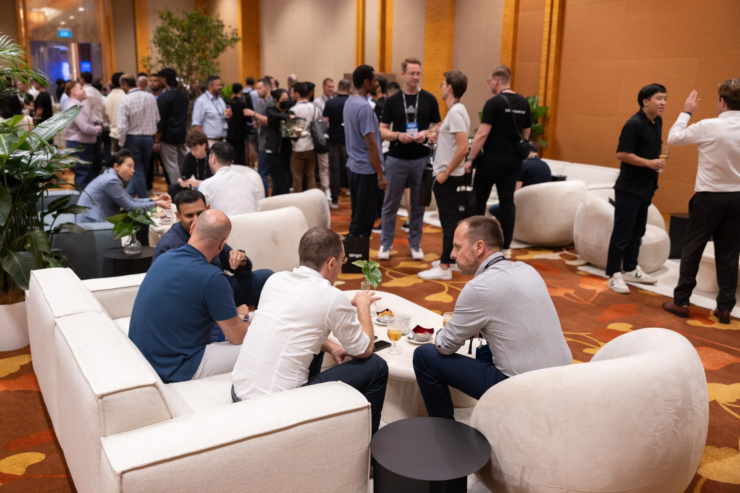  Networking lounge photograph featuring delegates relaxing and conversing on sofas surrounded by indoor greenery. 