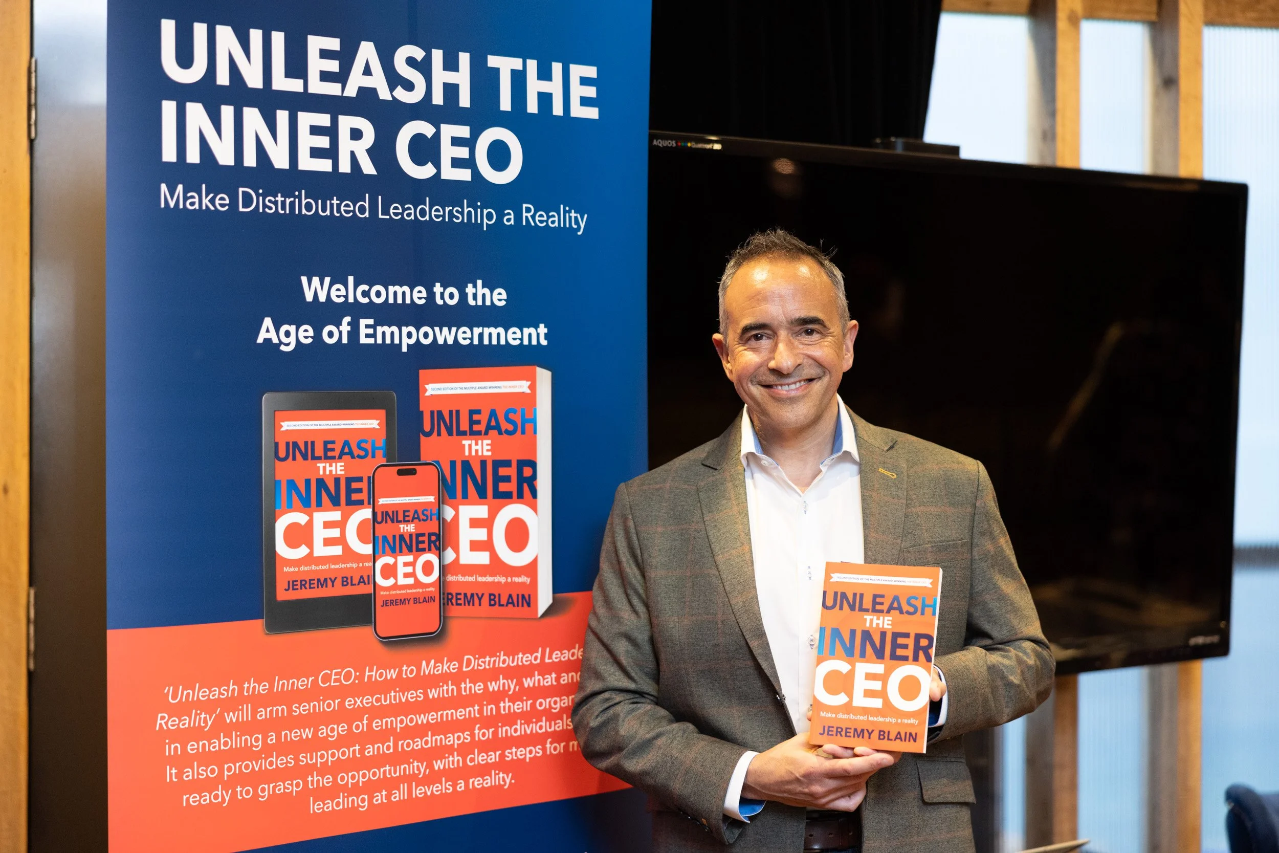  Author Jeremy Blain holding a copy of his book Unleash the Inner CEO next to the event banner. 