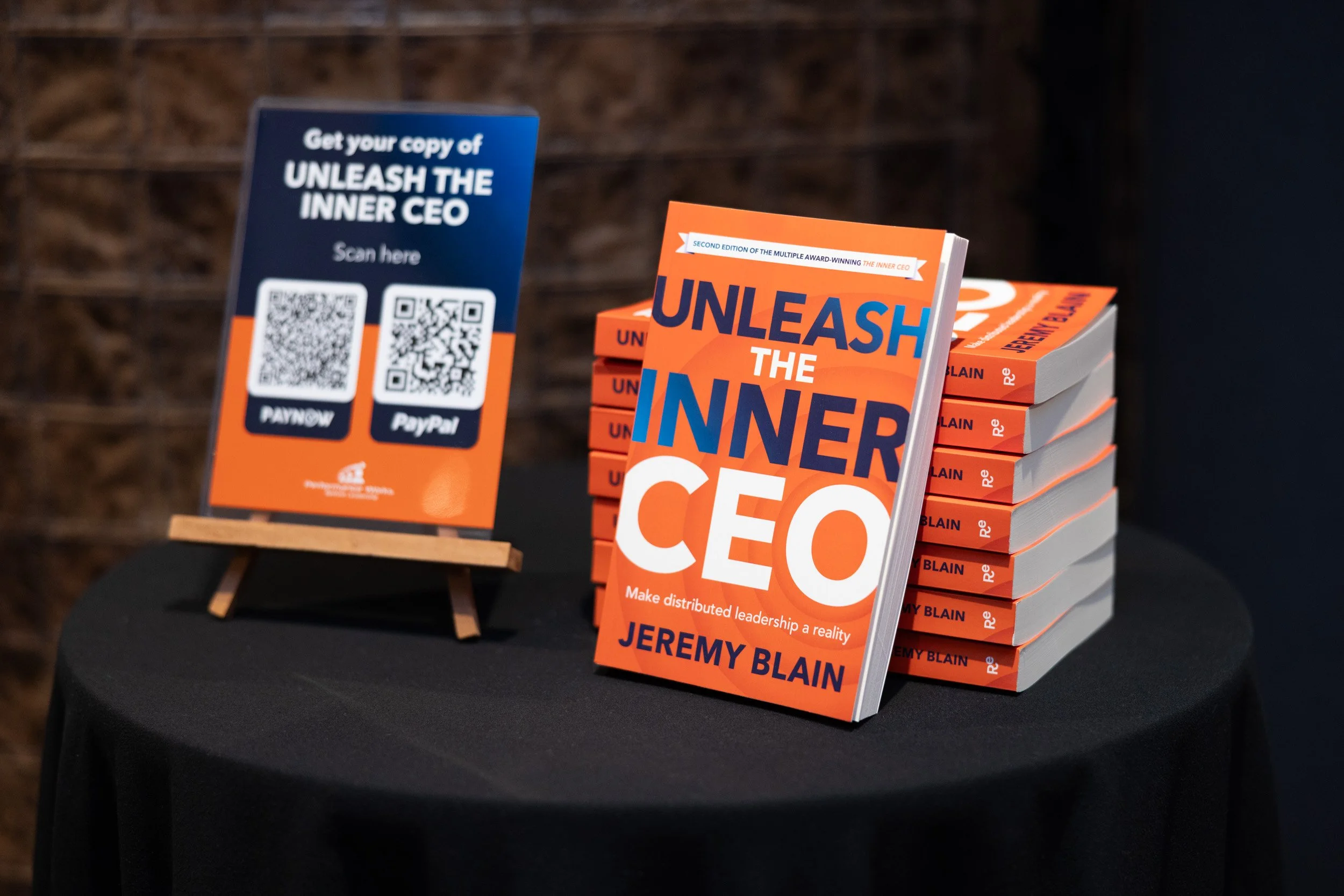  Stacked copies of Unleash the Inner CEO by Jeremy Blain on a display table with a QR code stand. 