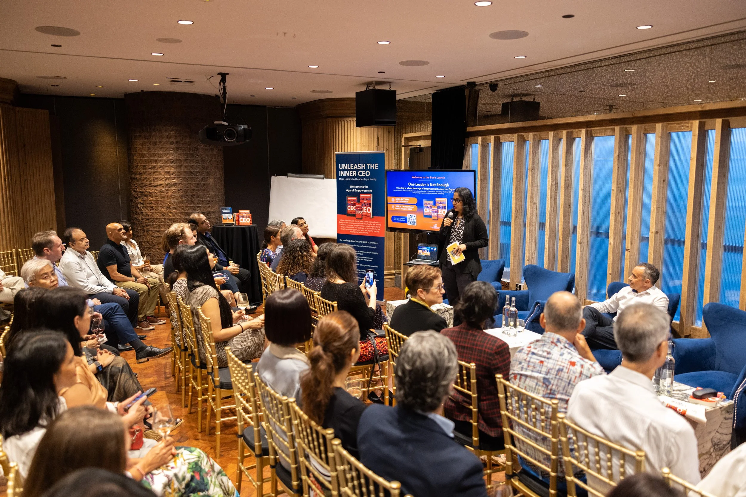  Wide angle shot of moderator Neha Thakkar addressing event attendees from the front stage. 