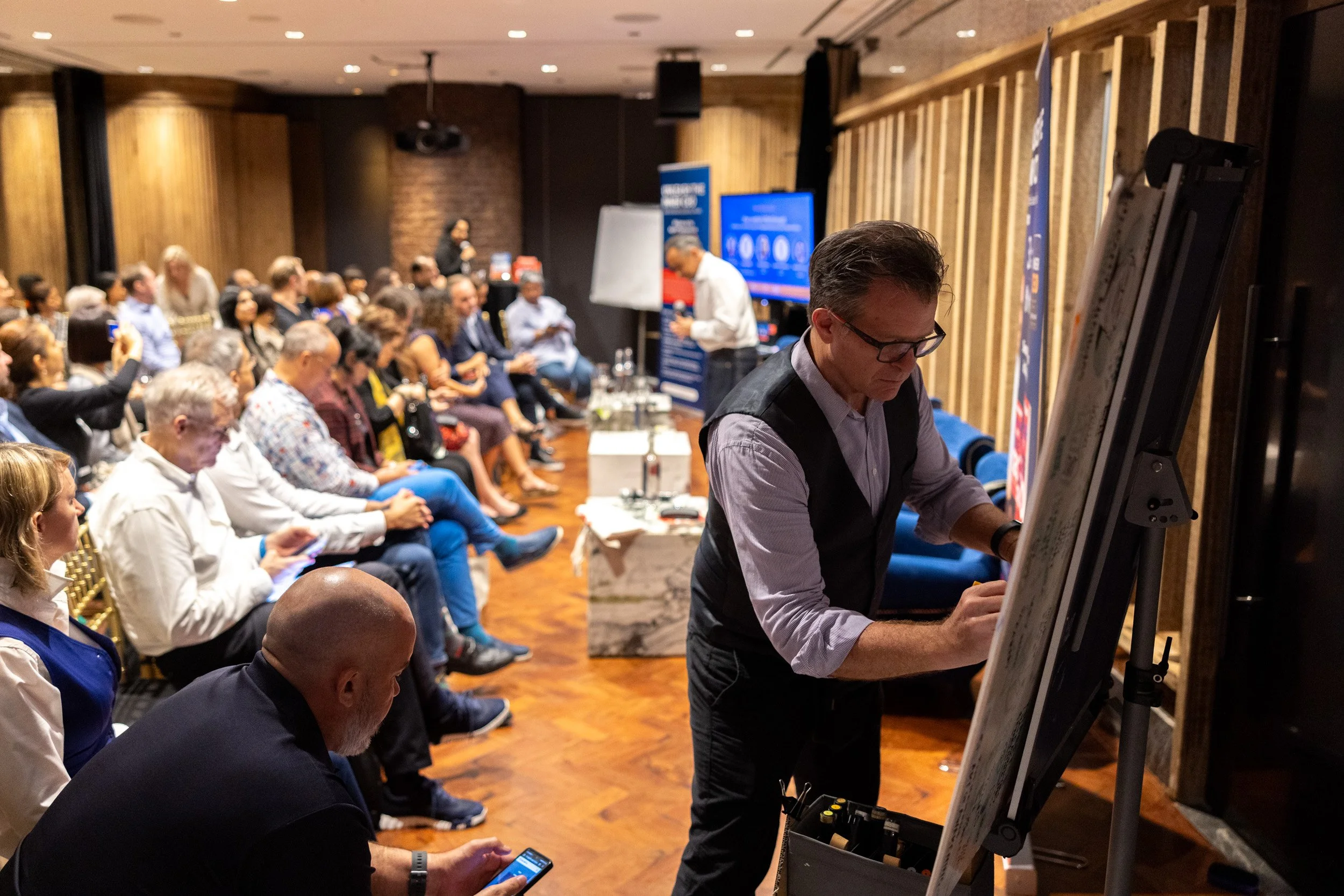  Angle view showing the graphic recording artist illustrating key presentation themes with attendees seen behid. 