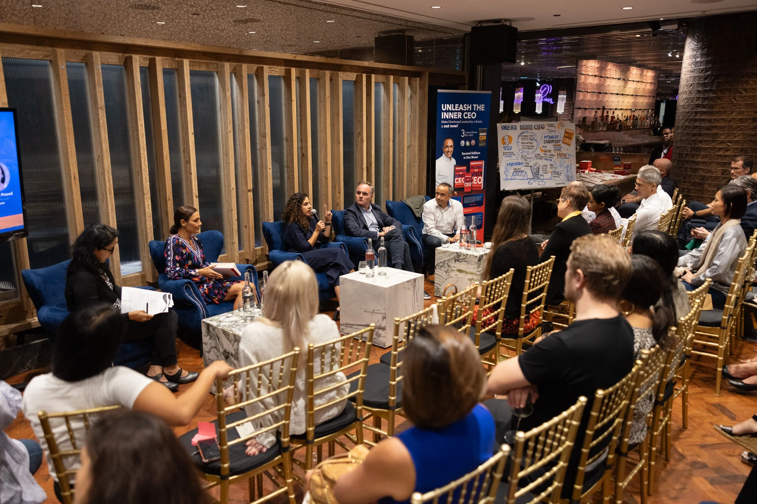  Stage view of panel speakers Bruna Fontes, Antonio Codinach, Natasha Prasad, and Jeremy Blain discussing distributed leadership. 