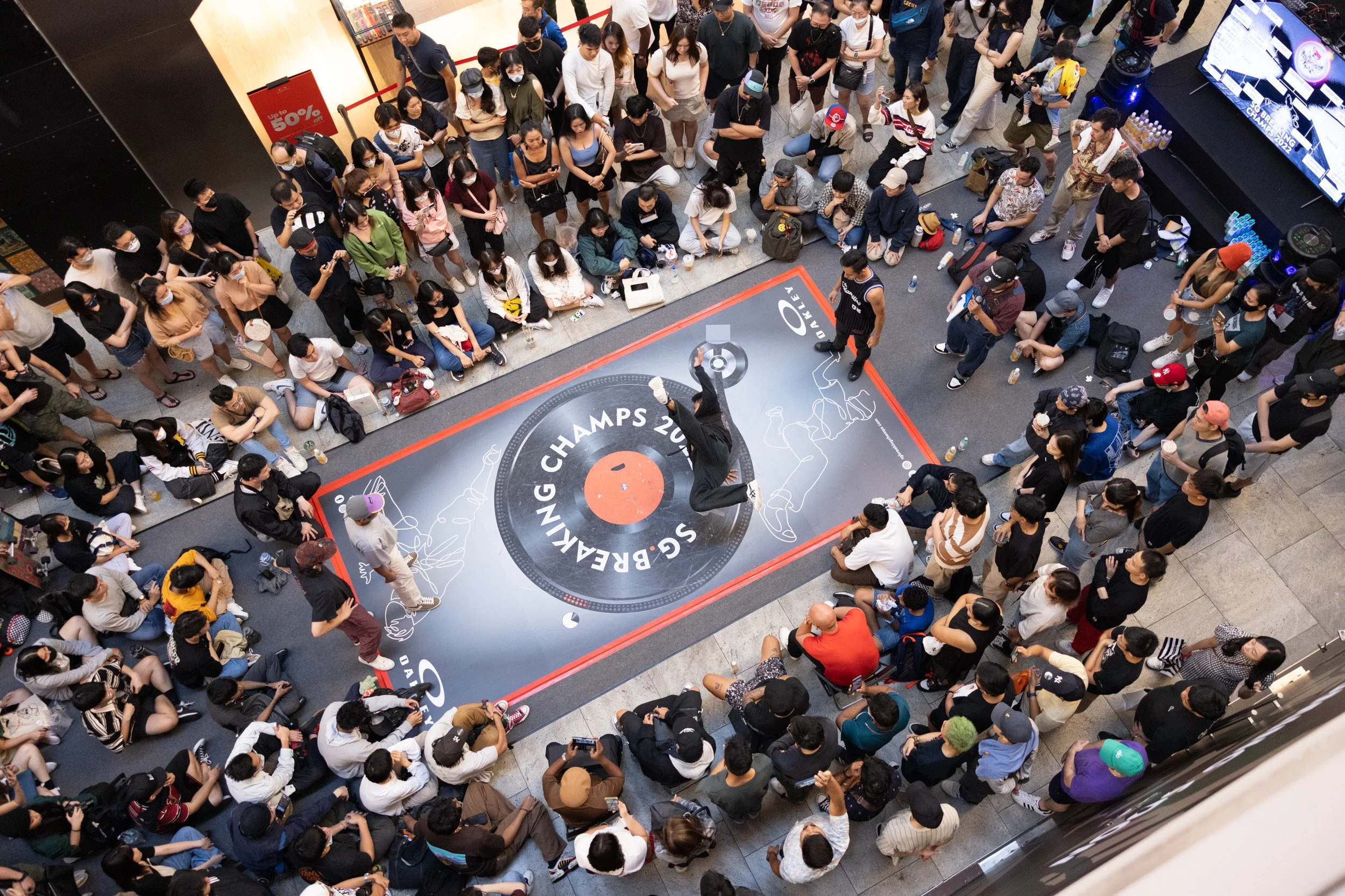  Top-down perspective from the second story capturing a breaker balancing in a single-hand freeze pose during the battle. 