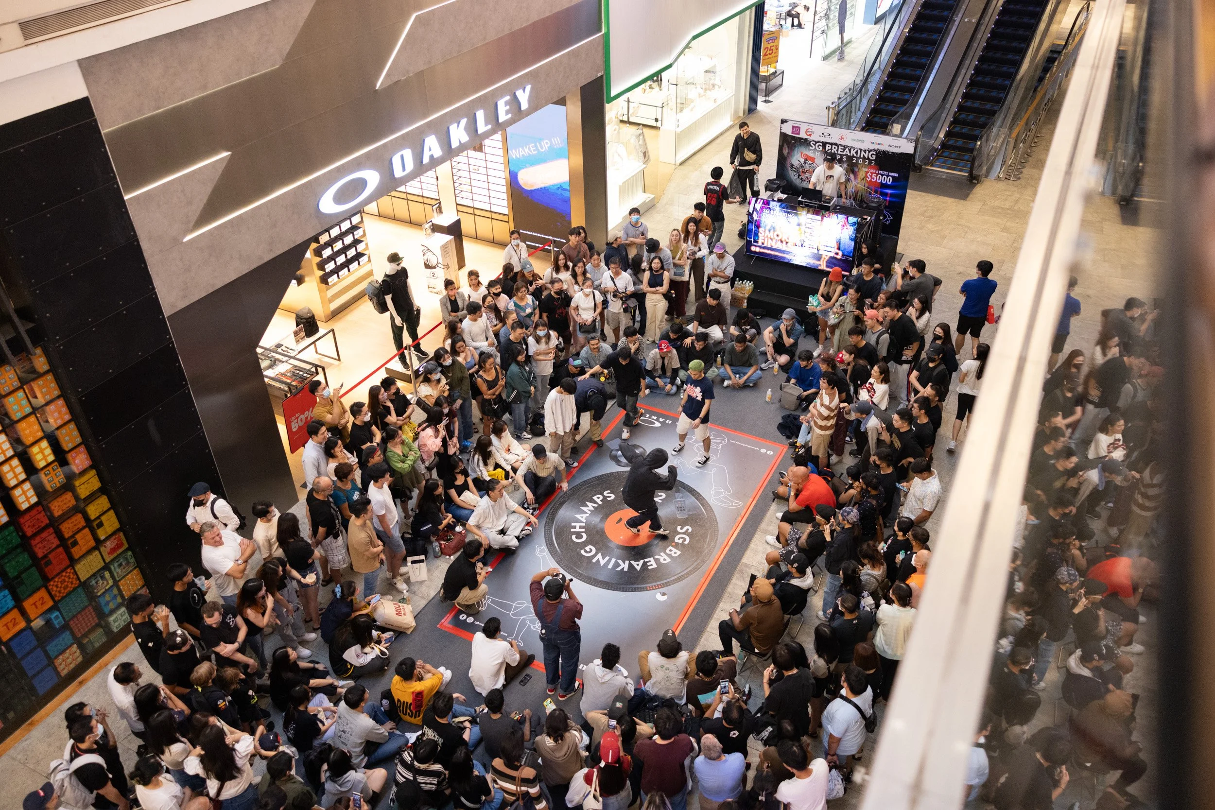  Wide upper-level photograph showing a street dancer performing top rock steps on the branded dance floor. 